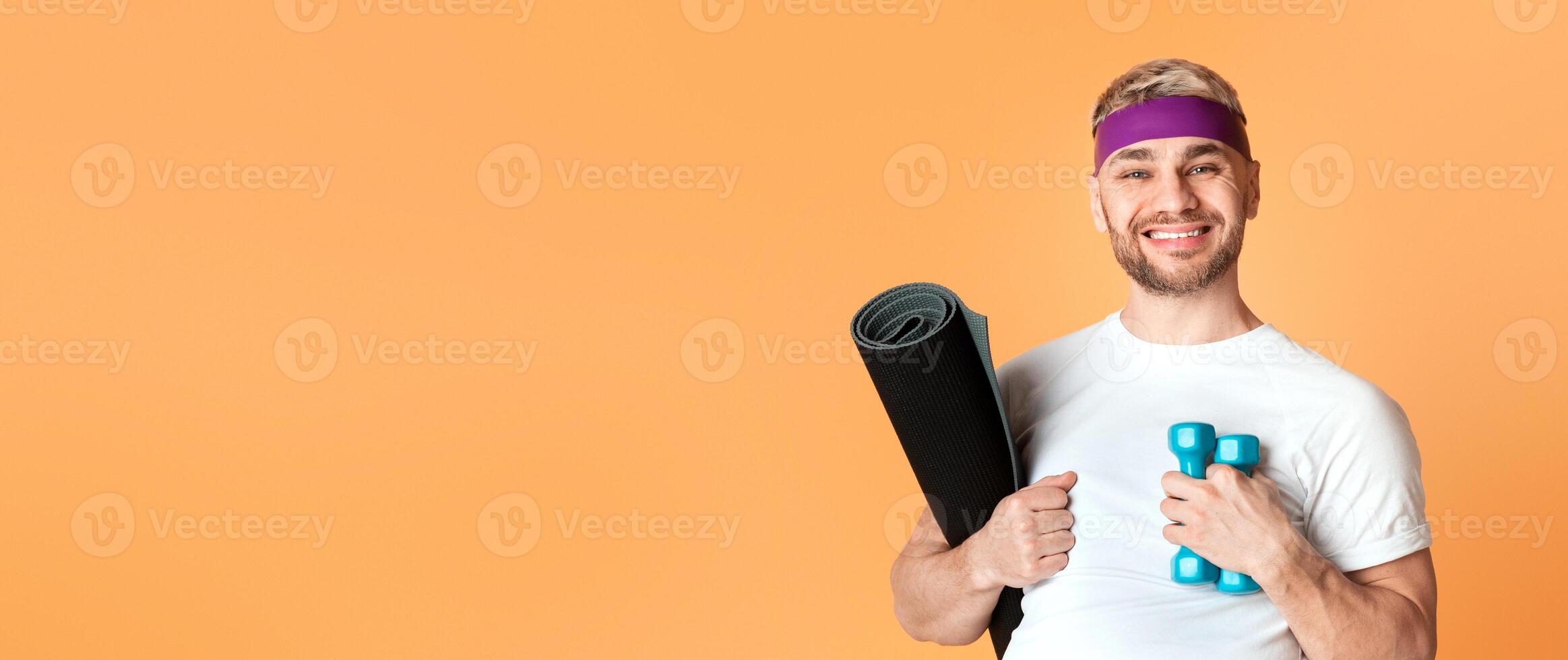 Young smiling man with dumbbell and fitness mat, free space photo