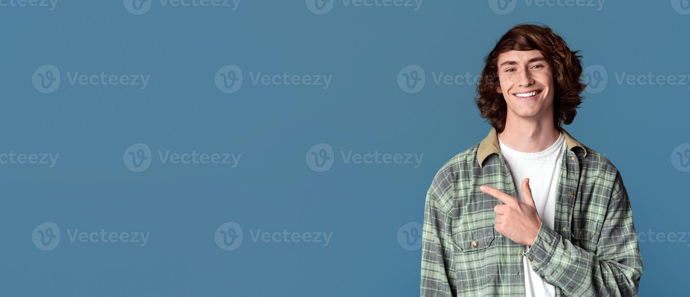 Confident teenager smiling and pointing aside on turquoise background, copy space photo