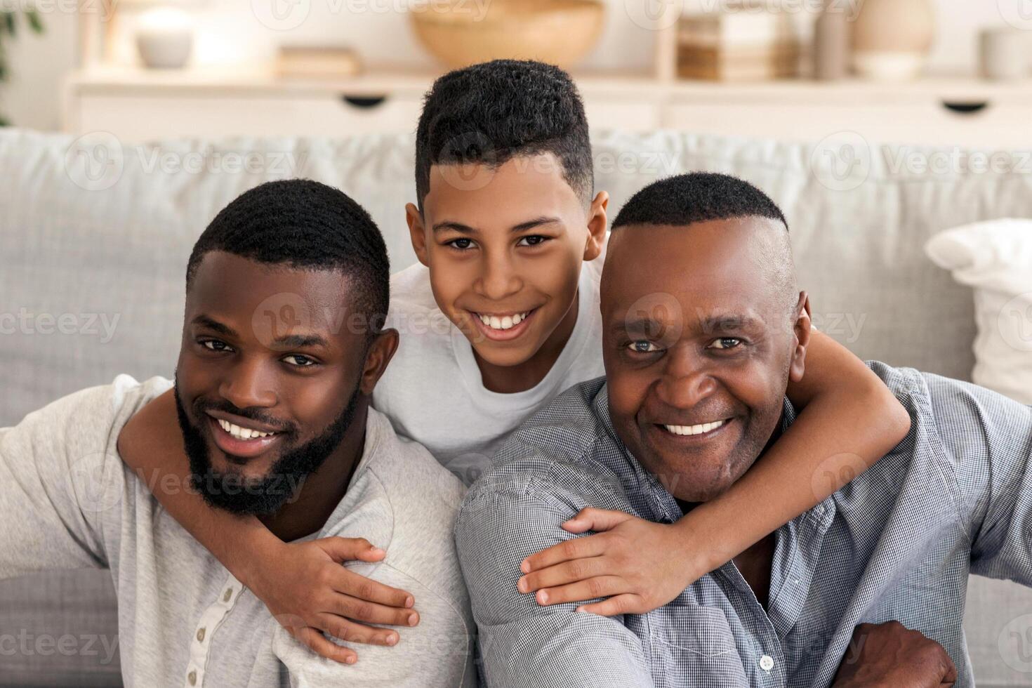 Portrait of happy black multi generation family at home. Son, father and grandfather posing indoors in living room, hugging and smiling photo