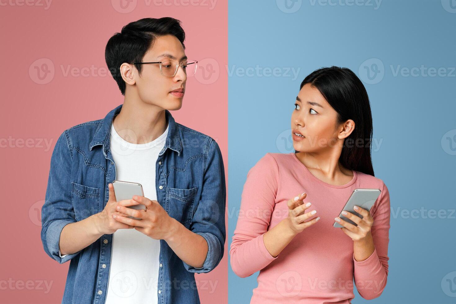 Curious asian man looking at his angry girlfriend mobile phone, gray studio background photo