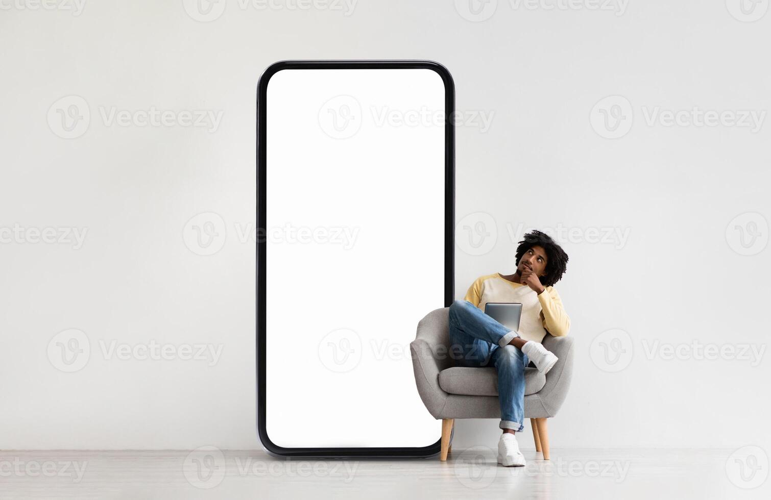 A person relaxes in a modern chair while contemplating, situated beside a giant smartphone-shaped screen. The indoor setting has a minimalist design and neutral tones. photo