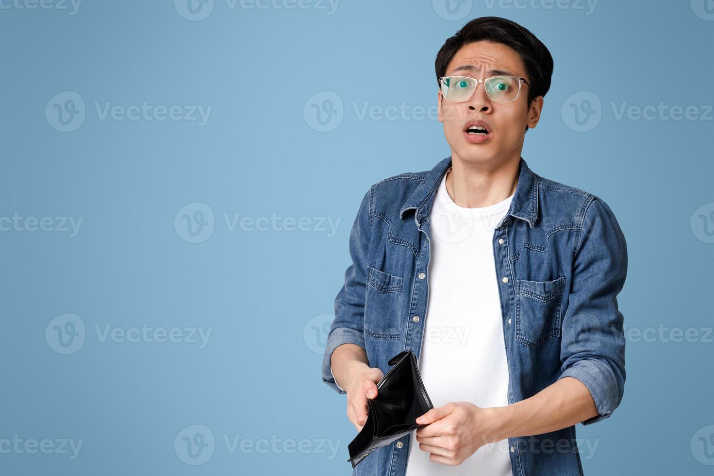 Poverty and absence of money. Unemployed sad asian guy showing empty wallet, looking at camera, standing over light studio background with free space photo