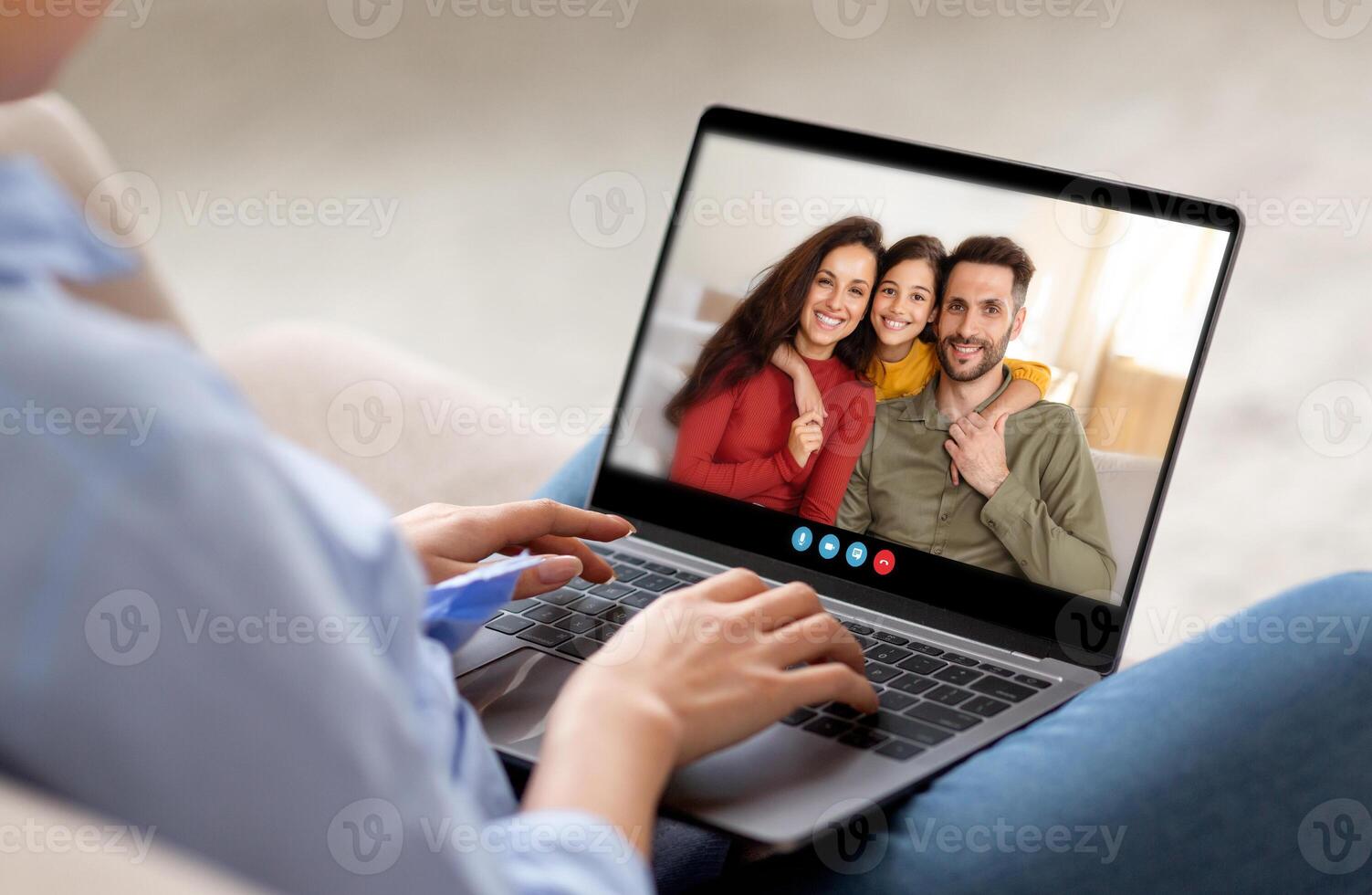 A person is engaged in a call with family members, smiling warmly while seated in a comfortable living area, creating a moment of connection and joy. photo