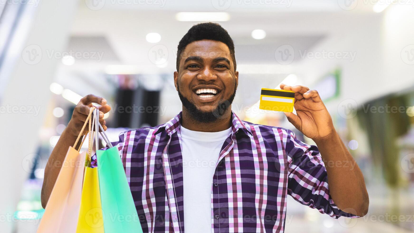 Easy Payment. Happy Black Man Holding Credit Card And Shopping Bags, Posing In Mall, Enjoying Seasonal Sales photo