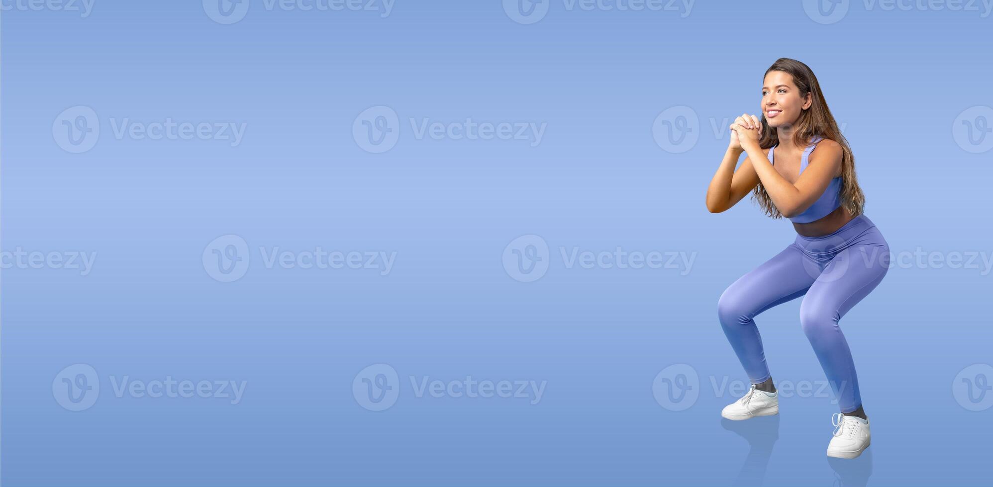 A woman is engaged in a squat exercise, showcasing her fitness routine. She wears a matching blue workout outfit and focuses on maintaining proper form while exercising. photo