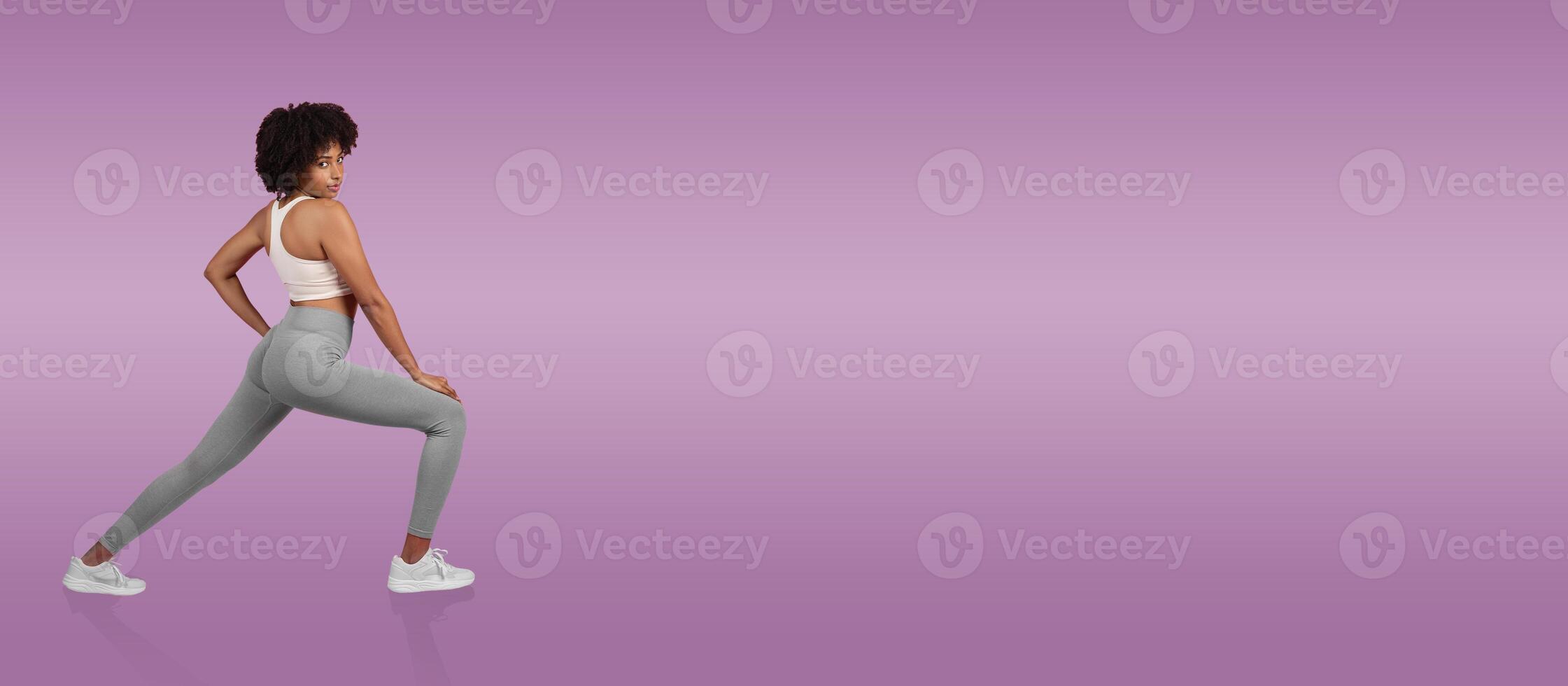 A young woman dressed in light gray leggings and a white sports top strikes a dynamic pose on a smooth purple background. She exudes confidence and energy in her stance. photo
