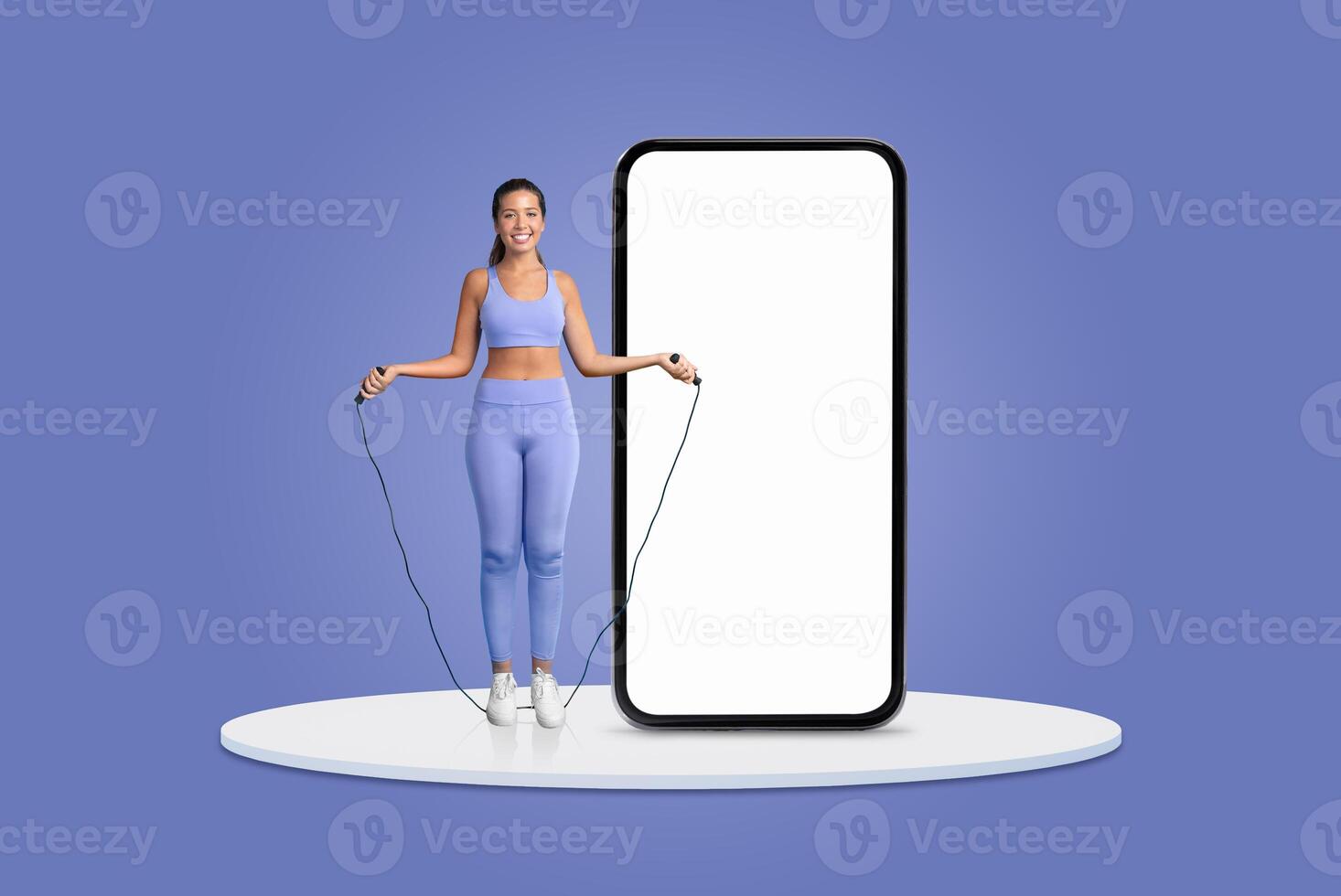 A young woman wears a matching athletic outfit while jumping rope beside an oversized smartphone display. The vibrant background emphasizes her energetic workout pose and enthusiasm for fitness. photo