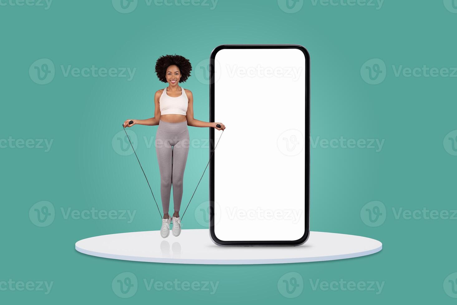 A woman jumps rope while smiling, showcasing her fitness routine beside a large blank smartphone display. The bright, minimalist background emphasizes her activity and enthusiasm for exercise. photo