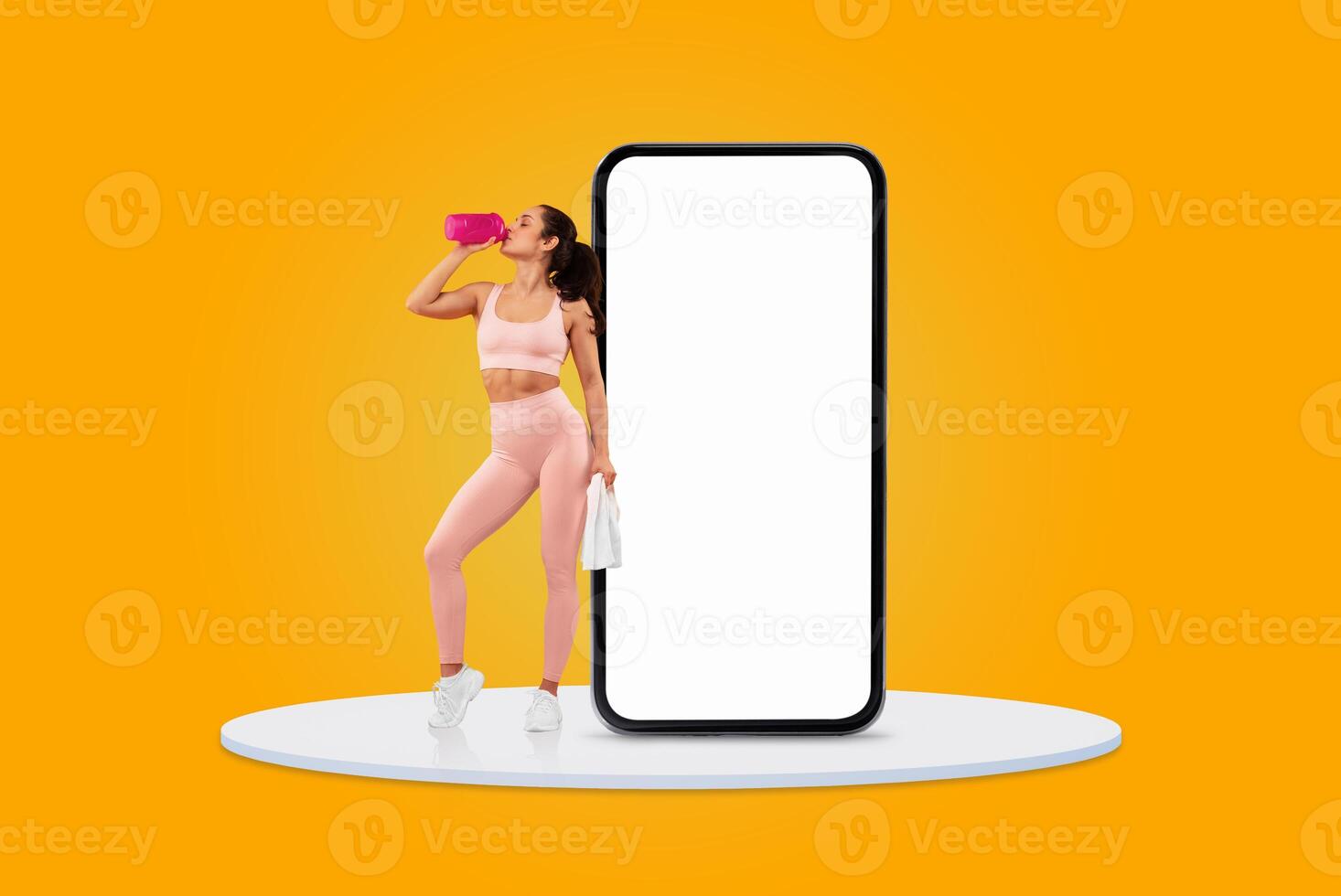 A woman dressed in pink athletic clothing stands confidently, sipping water from a pink bottle beside a large blank smartphone on a vibrant yellow background. photo