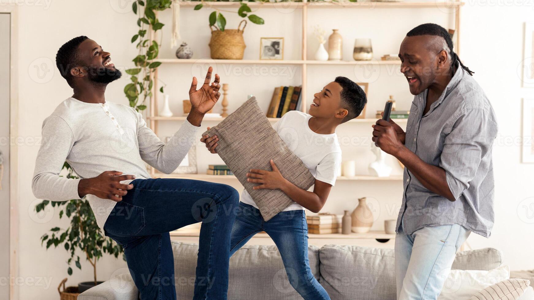 Black boy, his dad and grandfather having fun at home, dancing and singing in living room, enjoying spending time together photo