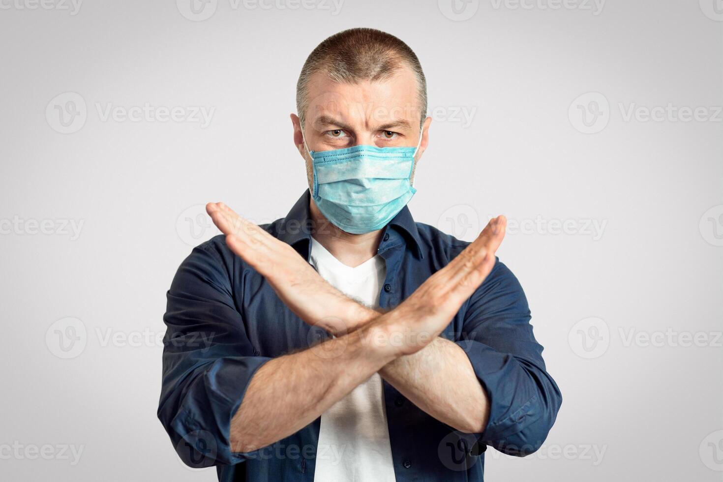 Coronavirus Restrictions. Man In Protective Medical Mask Crossing Hands Forbidding Something Standing Over Gray Studio Background. Panorama, Copy Space photo
