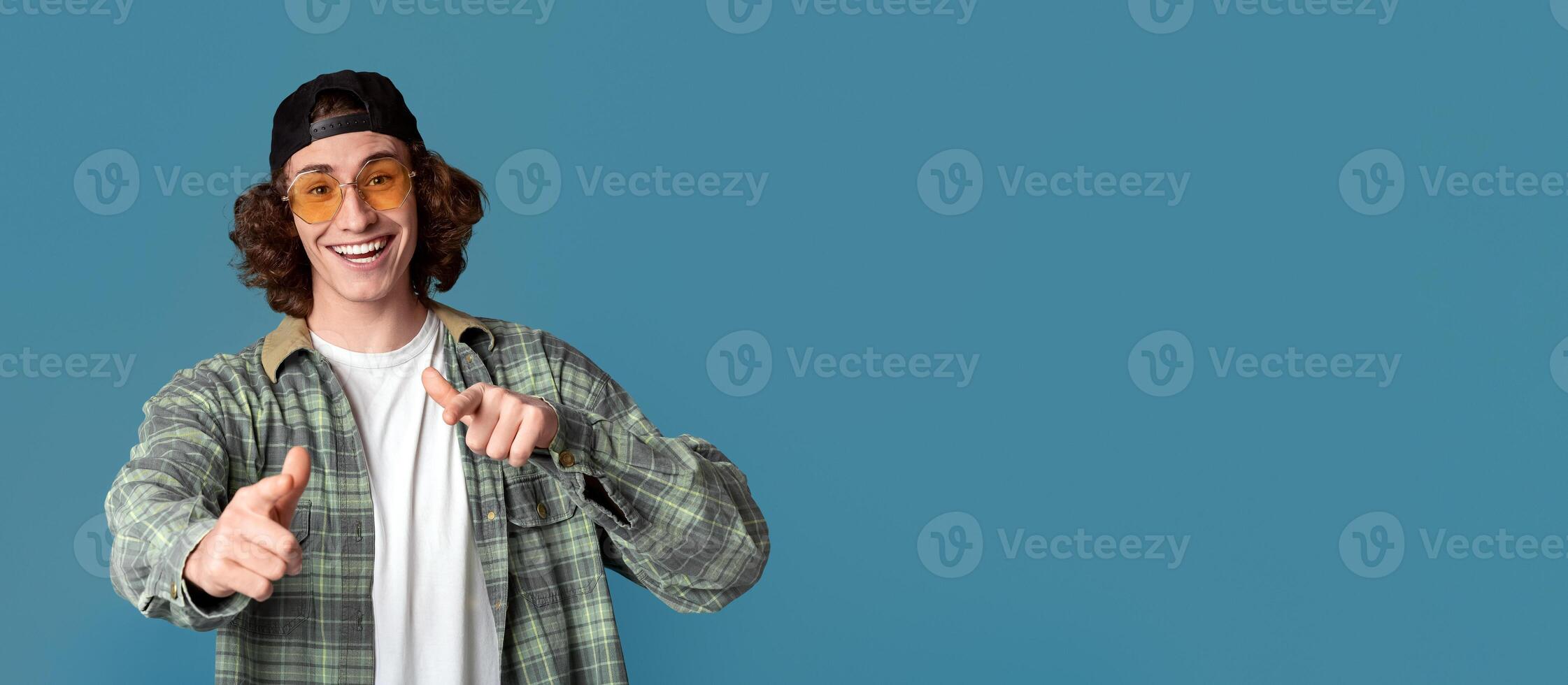 Portrait of cool young guy in sunglasses pointing at you on turquoise background photo
