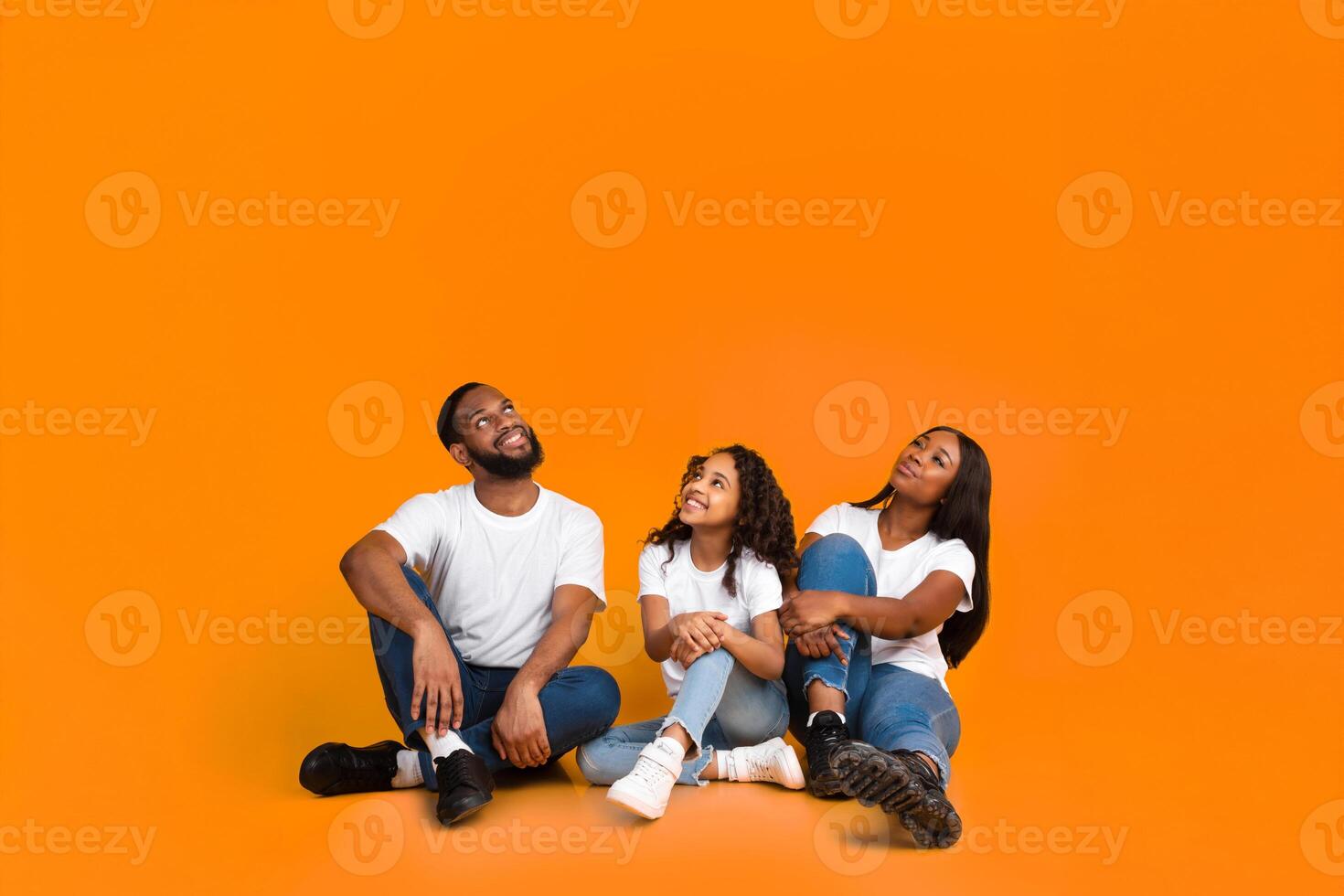 Free Place For Your Advert. Smiling African American Family Of Three People Sitting On The Floor, Looking Up At Empty Copy Space Isolated On Yellow Studio Background, Vertical Shot, Banner photo