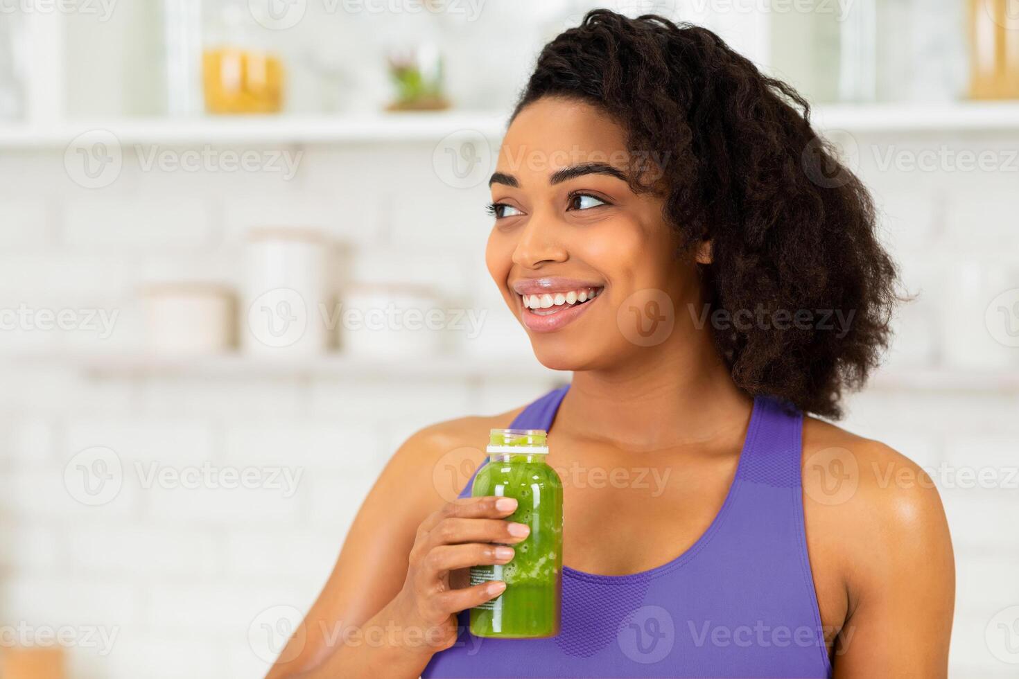 Detox Concept. Close up portrait of black girl holding bottle with homemade green juice, looking aside at free space photo