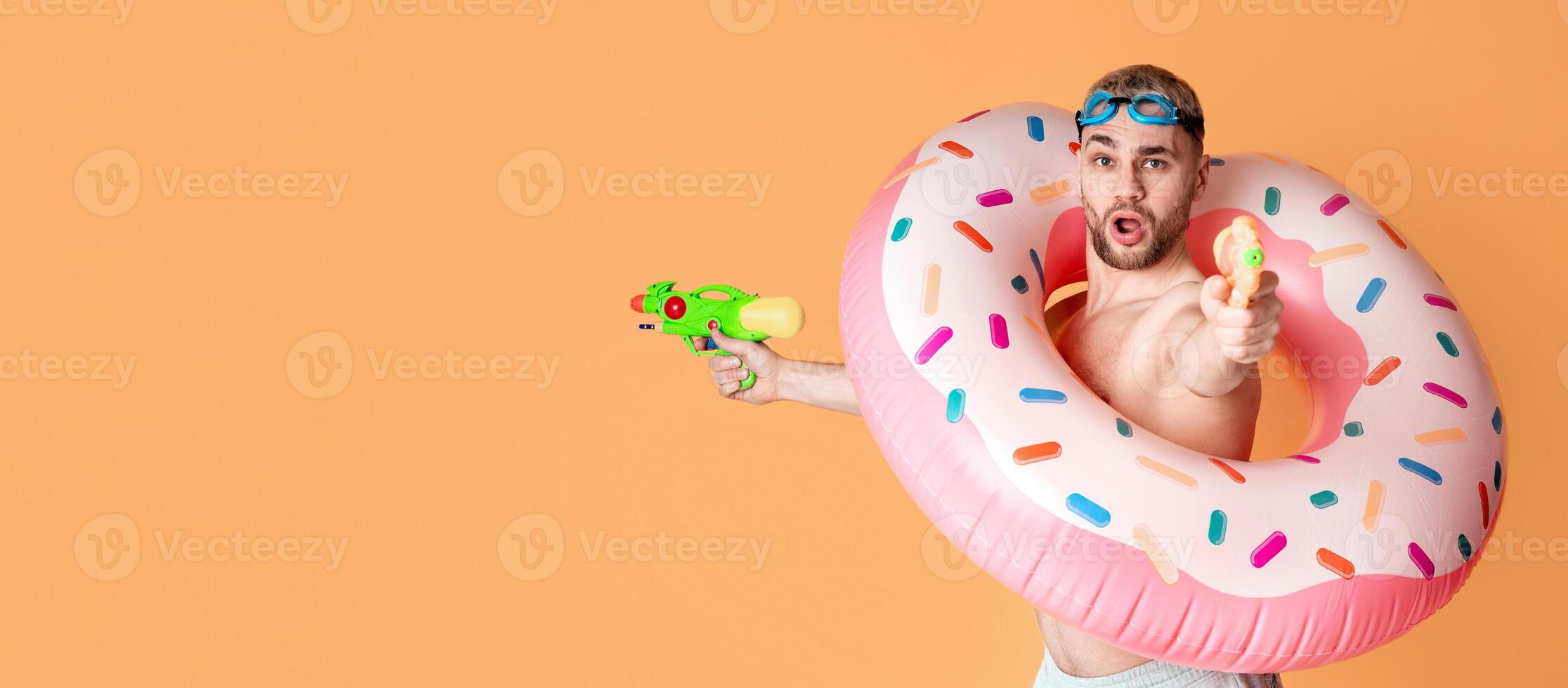 Expressive guy in inflatable ring shoots water guns with open mouth photo