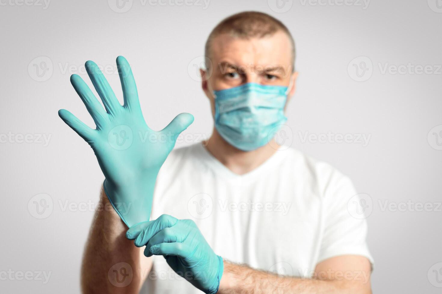 Virus Protection. Man In Medical Mask Putting On Rubber Gloves Standing Over Gray Background. Shallow Depth, Selective Focus photo