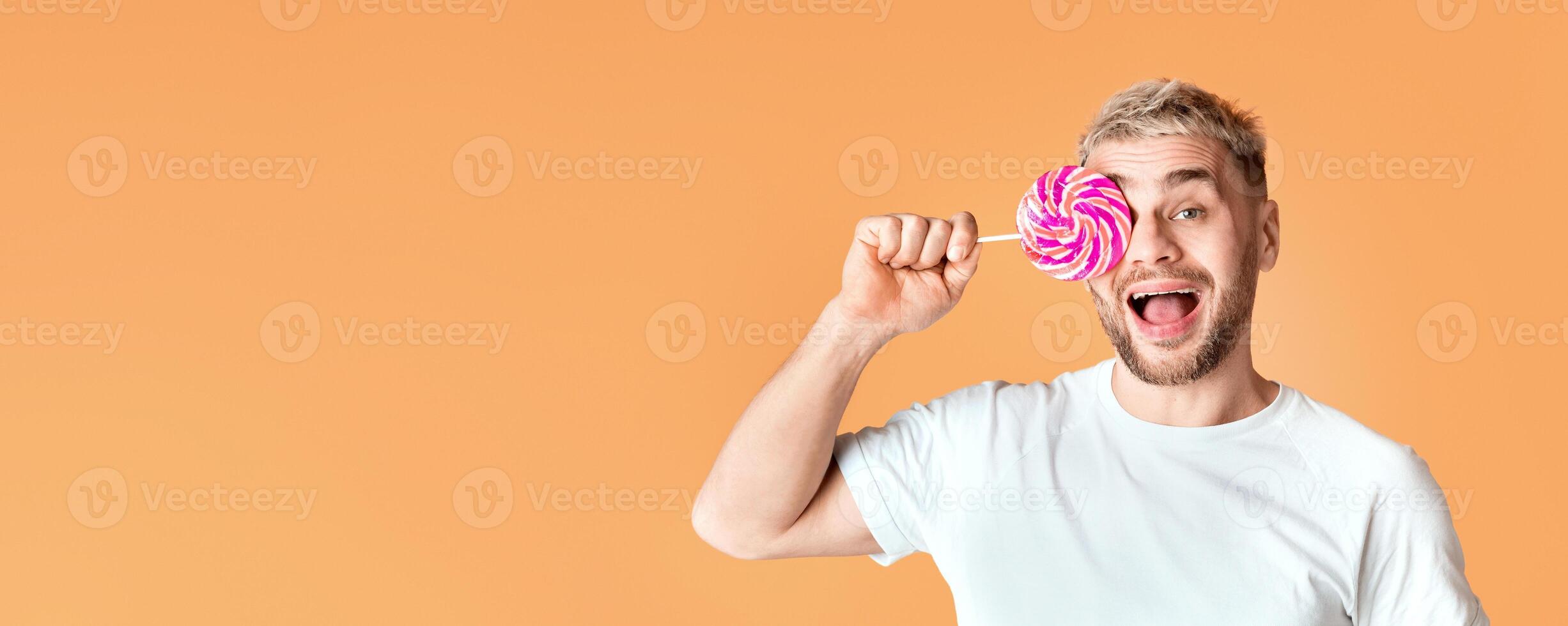 Happy millennial man with open mouth closes the eye with rainbow lollipop photo