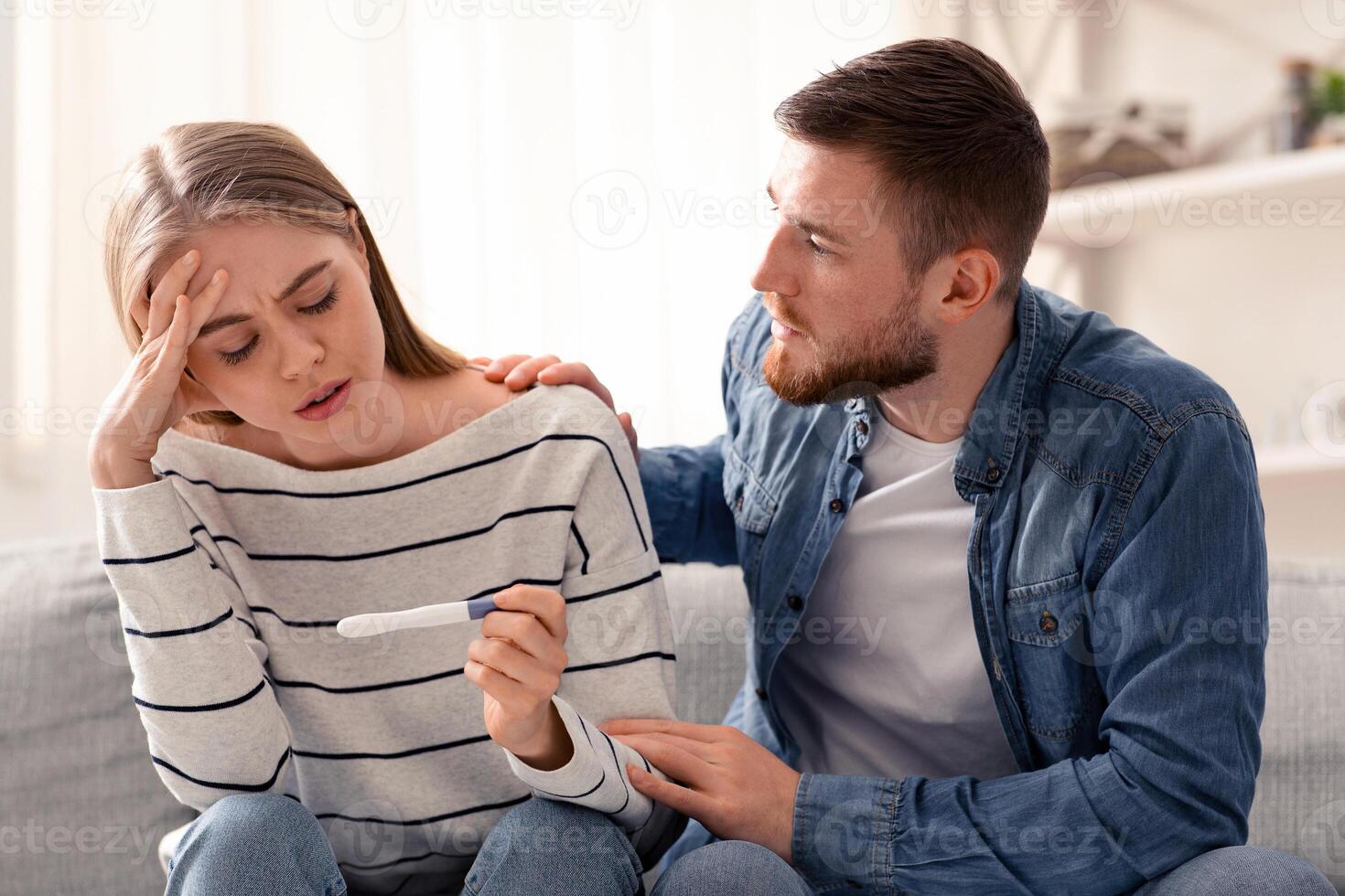 Couple dreaming to be parents. Upset man and woman looking at negative pregnancy test at home photo