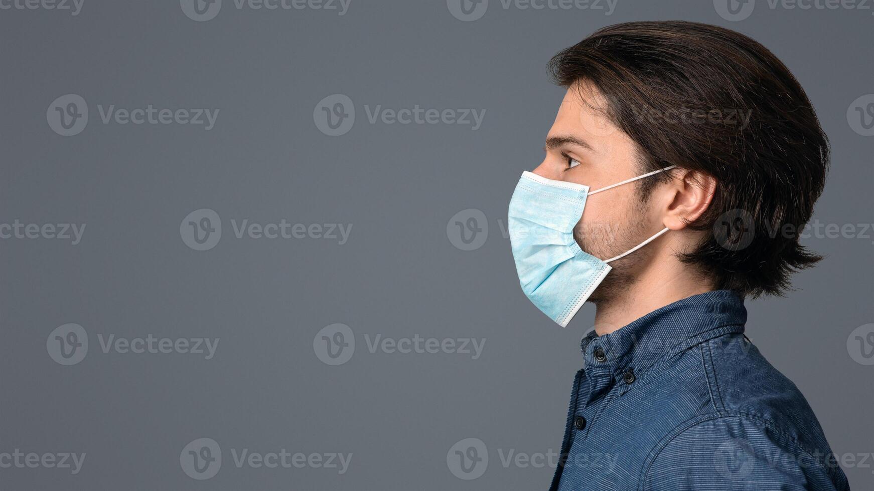 Profile portrait of millennial man wearing protective medical face mask and looking at copy space over light background photo