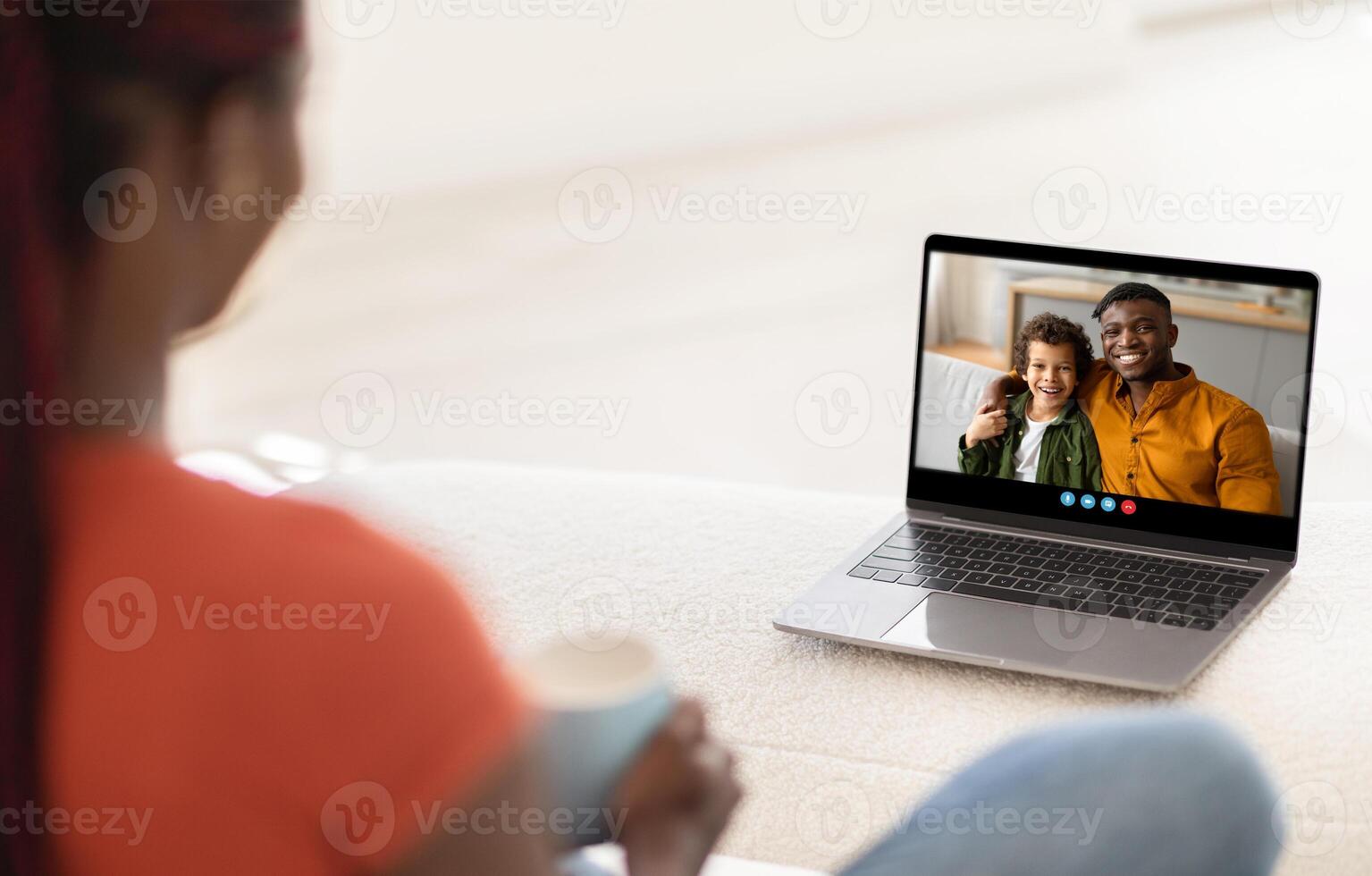 A mother enjoys a call with her smiling child, creating a moment of connection and joy. The warm light from the afternoon sun brightens their cozy living space. photo