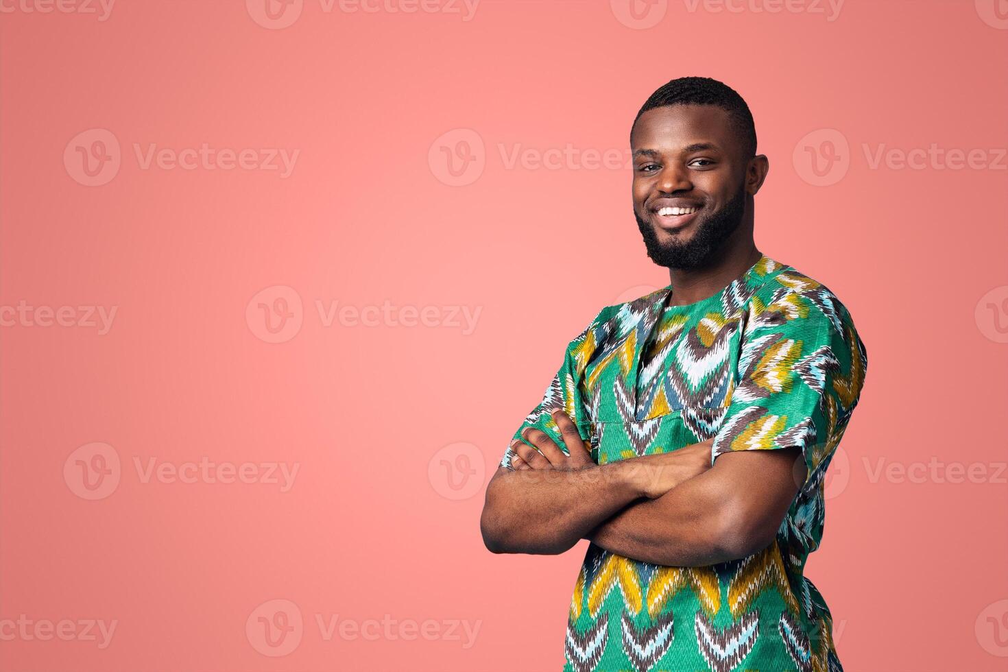 Confident black man smiling on blue studio background with empty space for advertisement. Happy african american guy in traditional costume standing with arms crossed, copy space photo