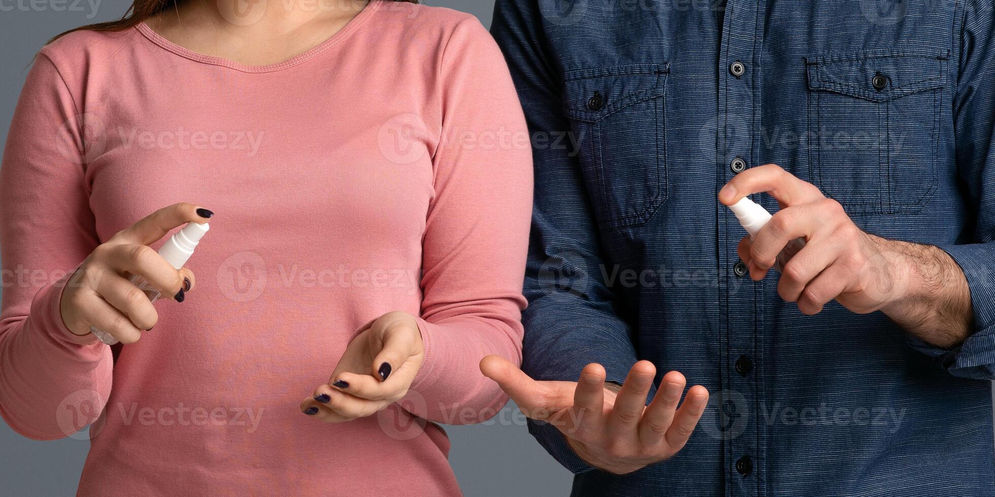 Precautions During Coronavirus Outbreak. Young couple applying disinfectant spray on hands to prevent spread of bacteria, light studio background photo