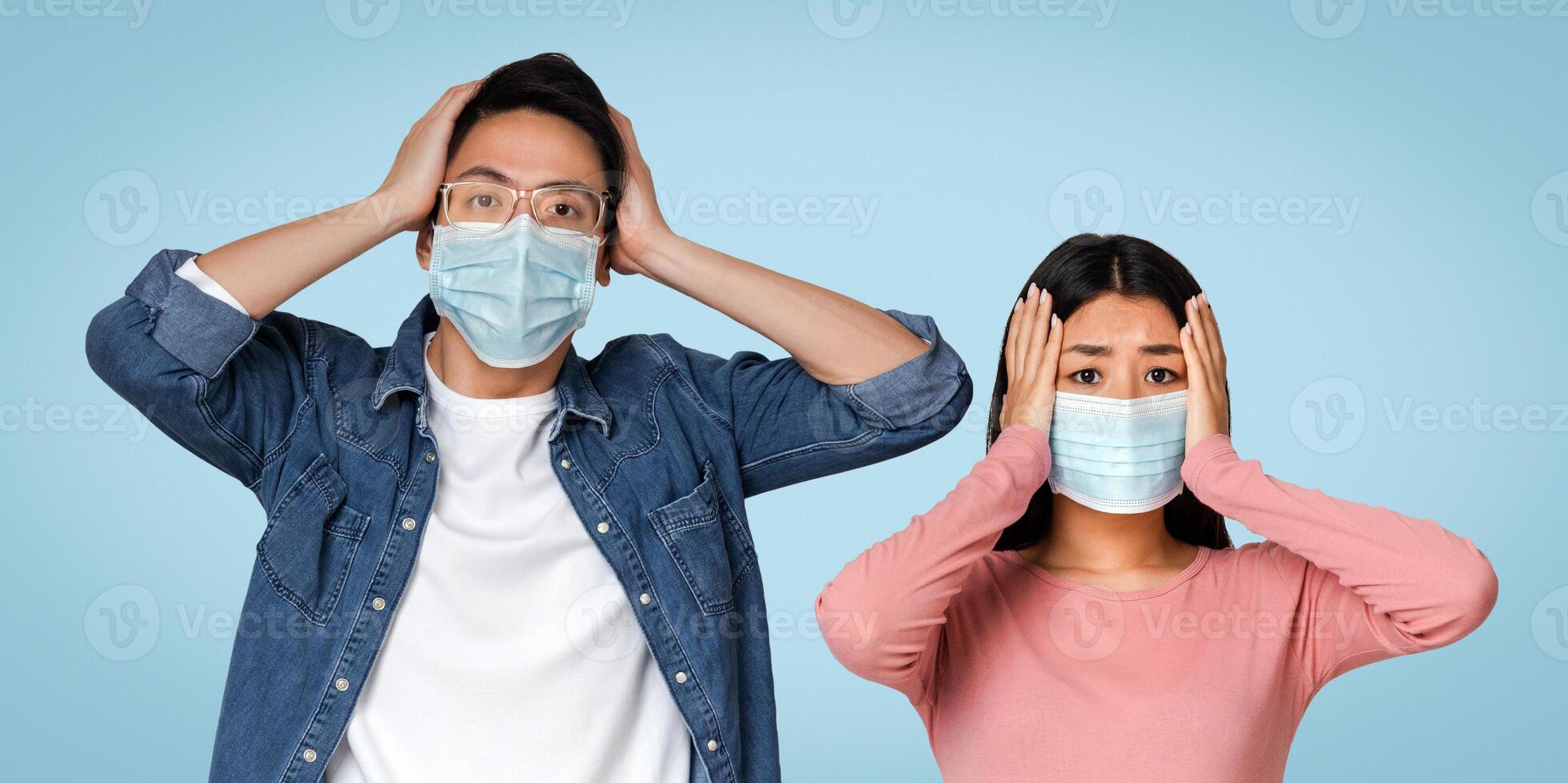 Coronavirus Panic. Asian Couple In Protective Masks With Scared Face Expression Holding Head With Hands, Emotionally Reacting To Virus Spread photo