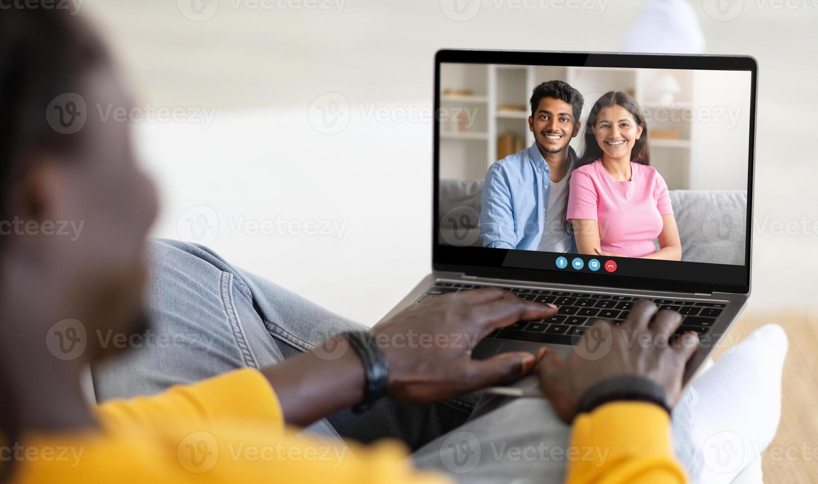 A person sits comfortably on a sofa, engaging in a call with two smiling friends. The bright room enhances the warm atmosphere of their conversation filled with laughter. photo