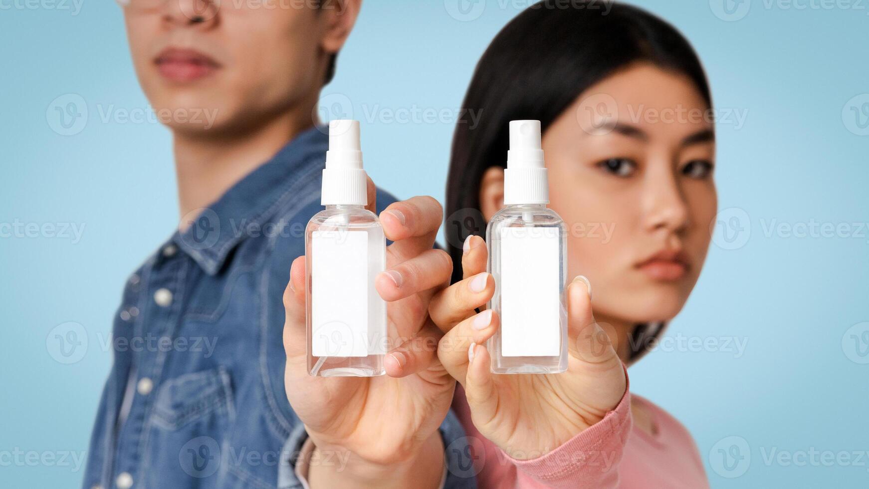 Bottles Of Sanitizing Sprays With White Sticker Label In Hands Of Chinese Couple, Light Studio Background, Selective Focus photo