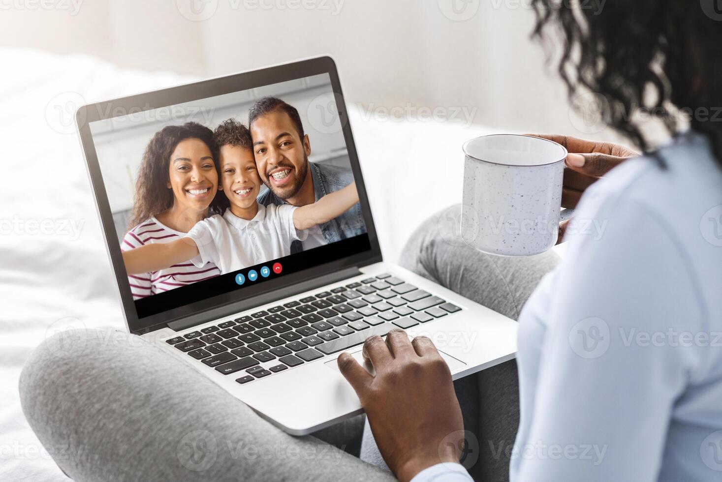 A person enjoys a call with family, smiling as they connect. The cozy atmosphere is enhanced by a warm drink while sitting comfortably on a bed in soft lighting. photo