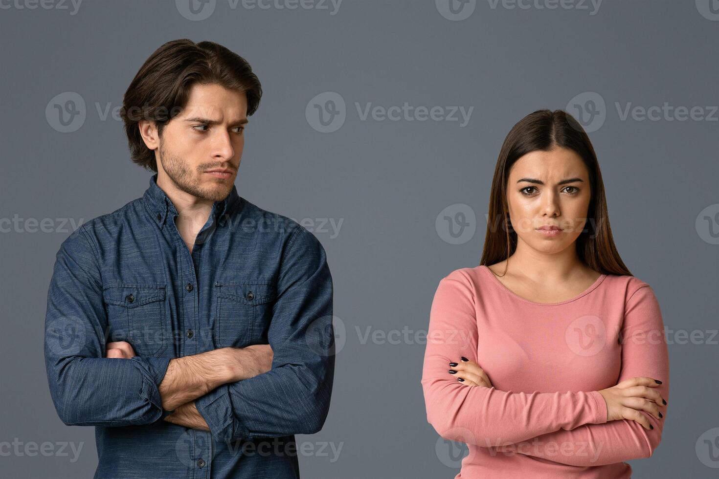 Young man looking with offence to his girlfriend after their quarrel, couple having relationship problems, light studio background with free space photo