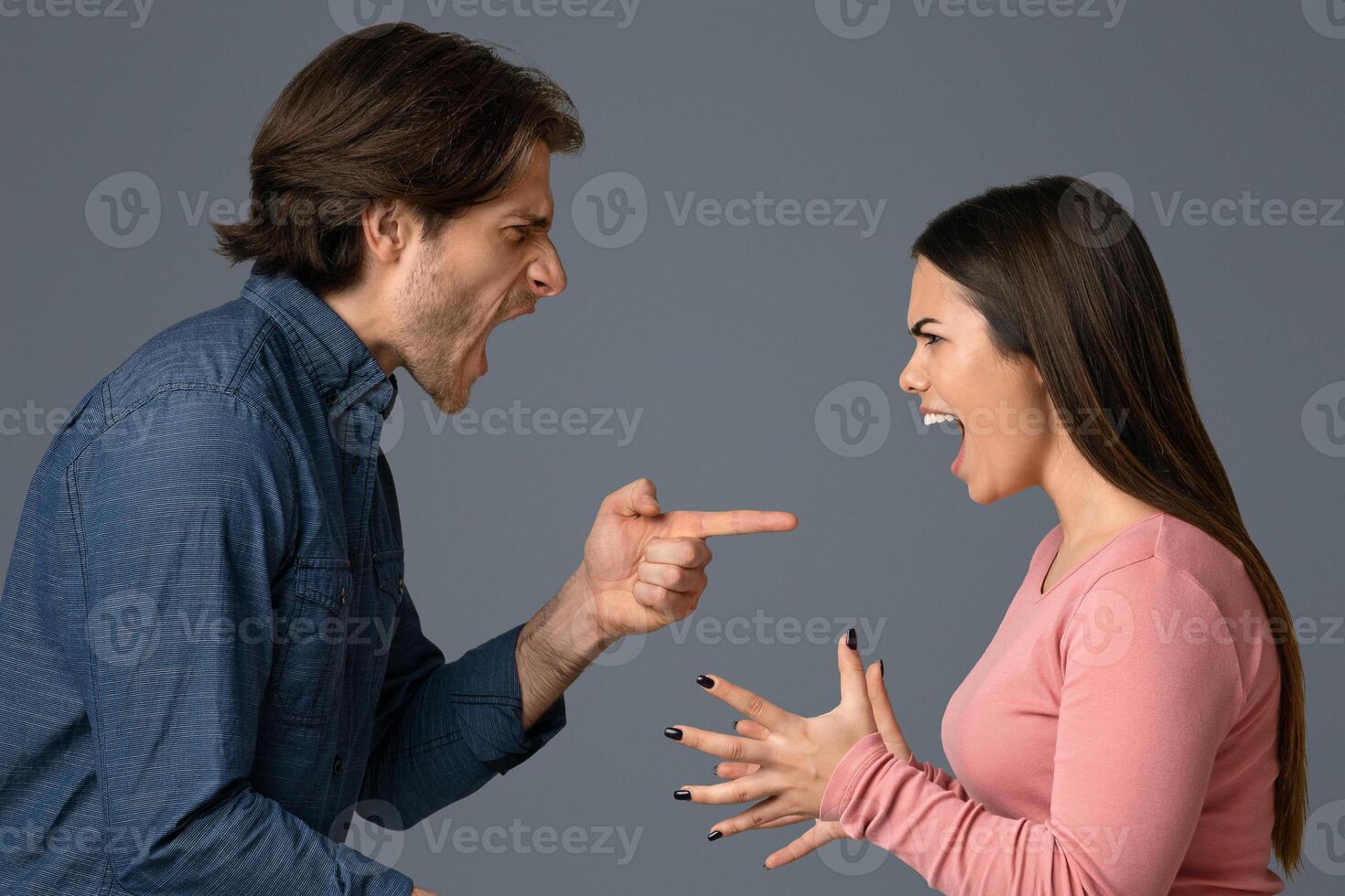 Millennial couple quarreling, shouting and blaming each other, having relationship problems, standing over light studio background, side view photo