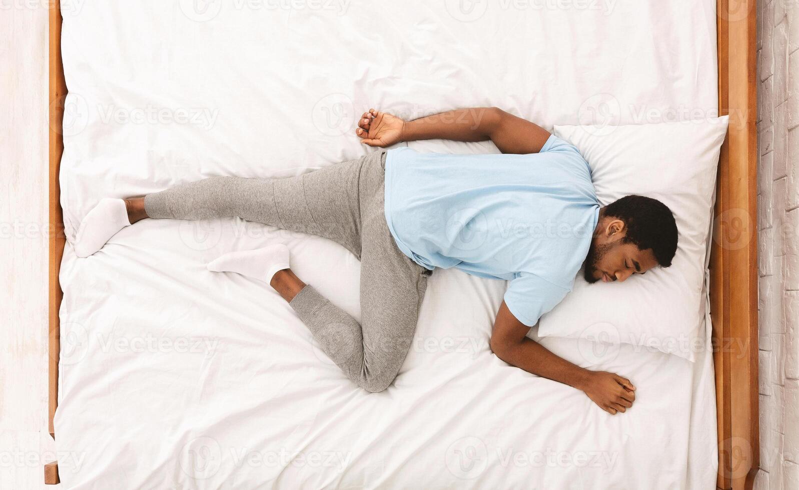 Comfortable pose for sleep. Black millennial guy sleeping, lying on stomach in bed, top view photo