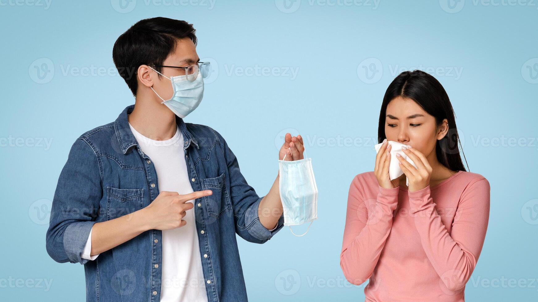 Fighting Virus Outbreak. Caring Asian Guy Offering Medical Face Mask To His Sick Girlfriend With Runny Nose, Standing On Light Background, Free Space photo