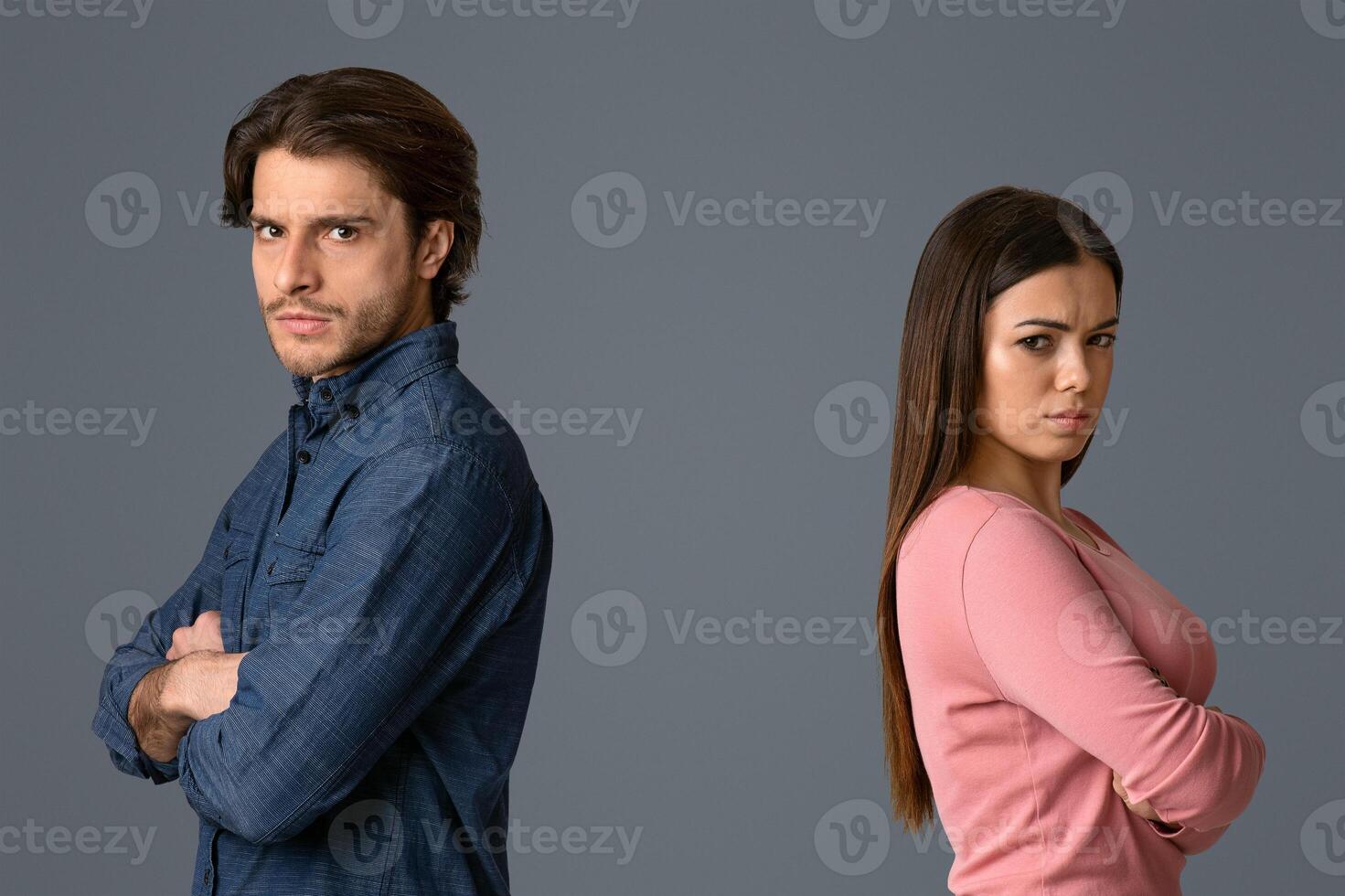 Break Up. Offended man and woman standing back to back with folded arms on light studio background and looking at camera, free space photo