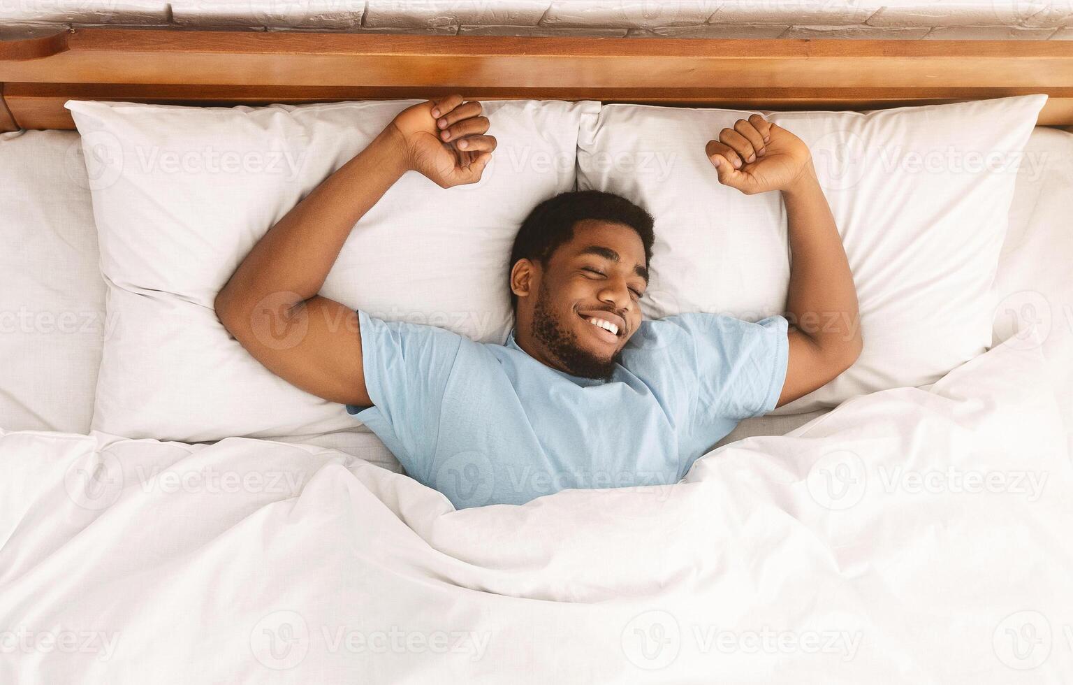 Comfortable sleep. Smiling african-american millennial guy sleeping, sprawled in bed, top view photo