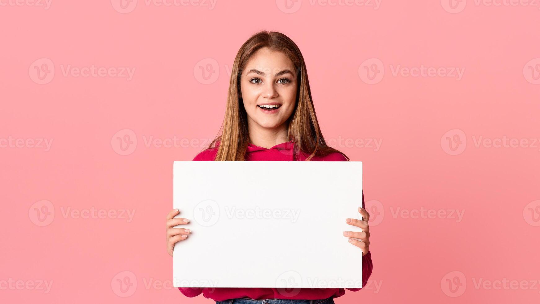 Something new. Happy smiling teenage girl holding white sheet of paper in hands with empty space isolated on pink background, studio shot photo
