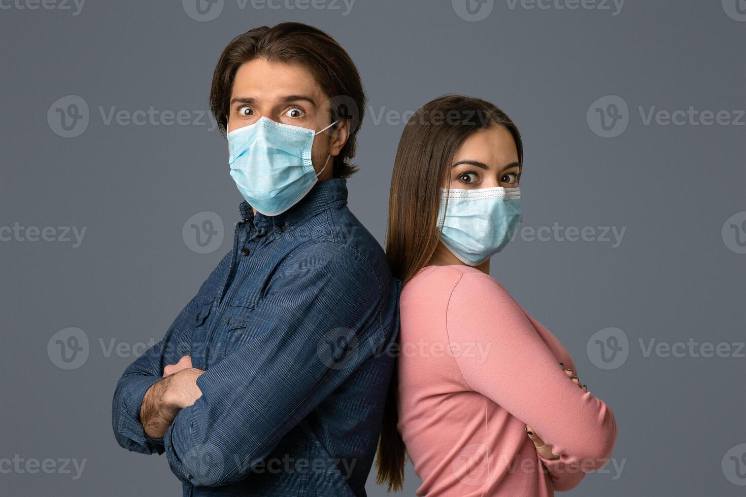 Millennial Couple In Protective Face Masks Standing Back To Back With Scared Face Expressions Over Light Background In Studio, Copy Space photo
