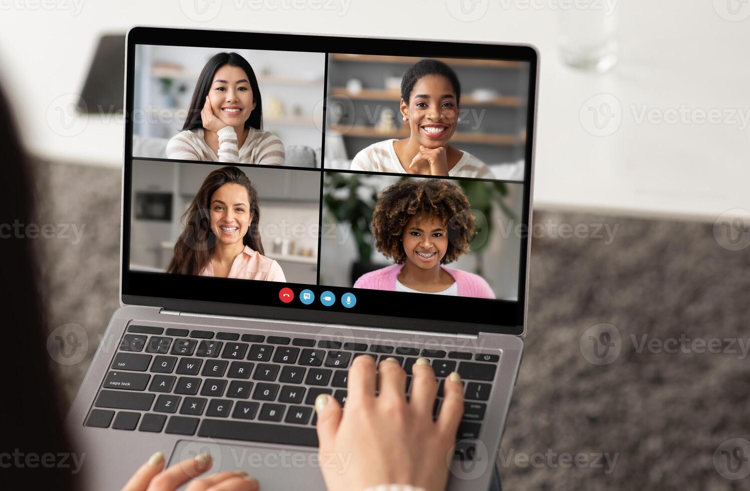A group of four women smiles at each other during a virtual meeting on a laptop. The setting is bright and cozy, showing a modern workspace. photo