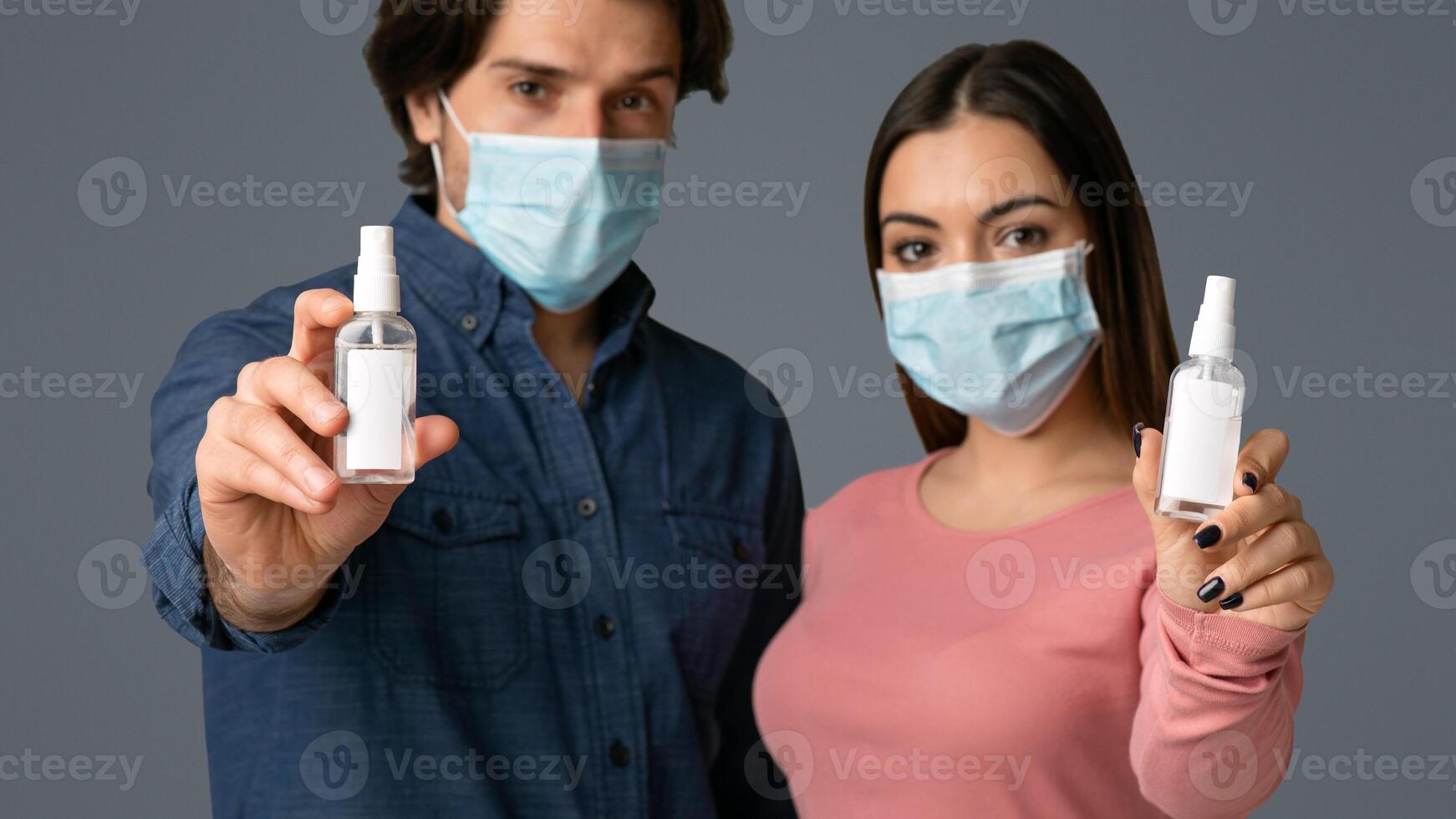 On Guard Of Disinfection. Bottles With Antibacterial Sprays In Hands Of Man And Woman In Medical Masks, Standing Over Light Background, Free Space photo