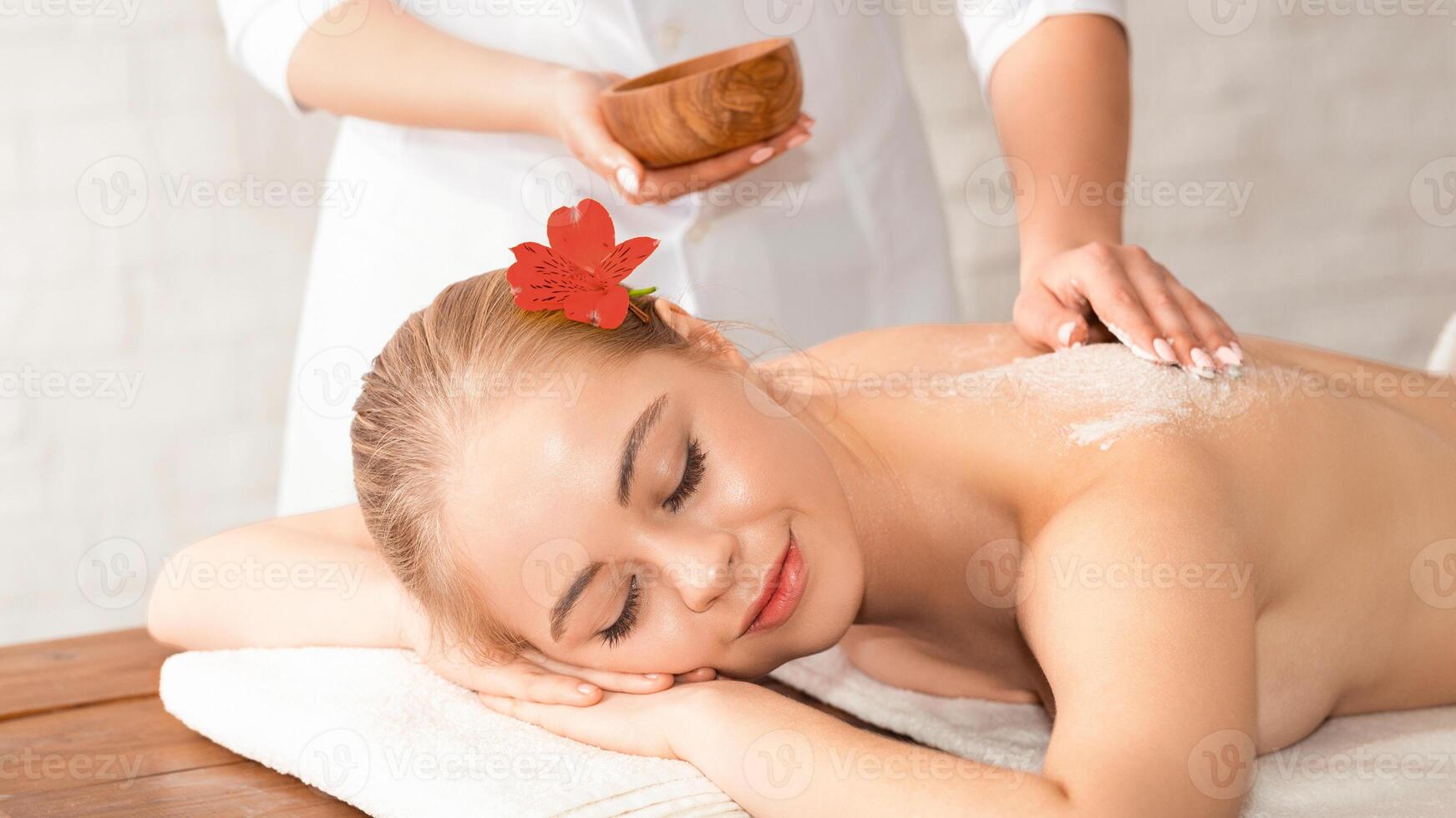 Smiling relaxed girl lying on table and takes massage with salt and body care in spa photo