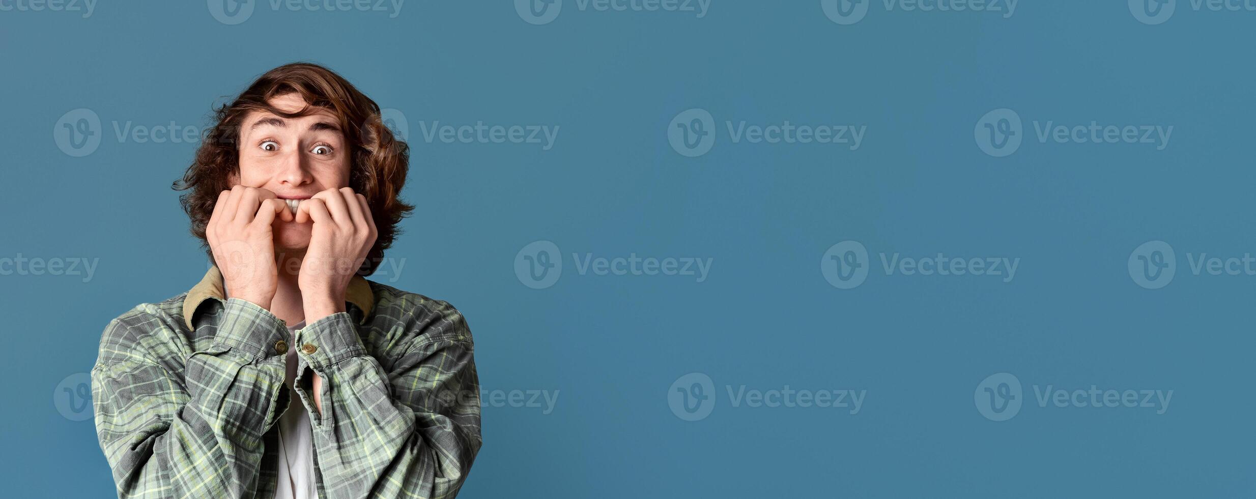 Curly teenager biting his nails in fear on turquoise background photo