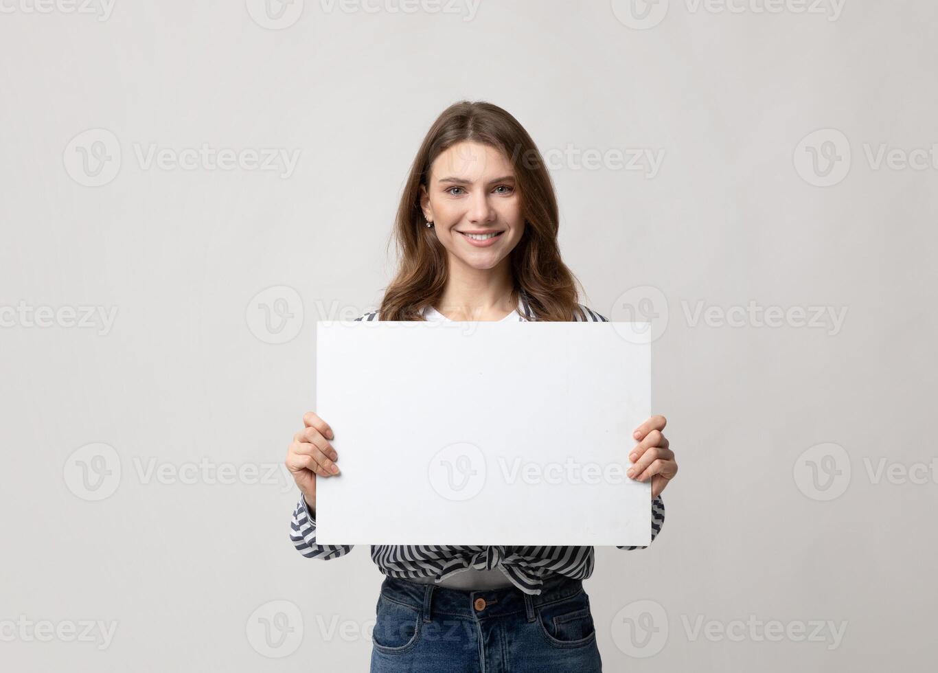 Beautiful Young Woman Holding Blank Placard With Copy Space For Advertisement. Smiling millennial lady demonstrating white empty billboard with place for text, standing over grey studio background photo