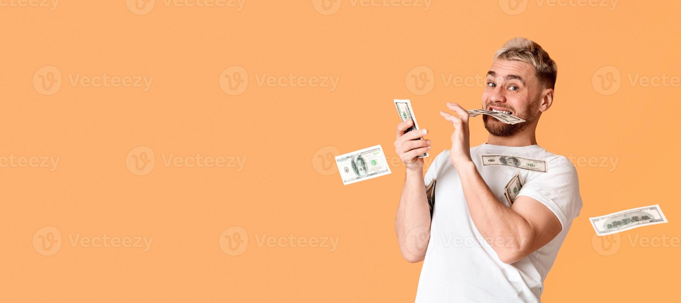 Glad guy holds banknote in his teeth and scatter money, panorama photo