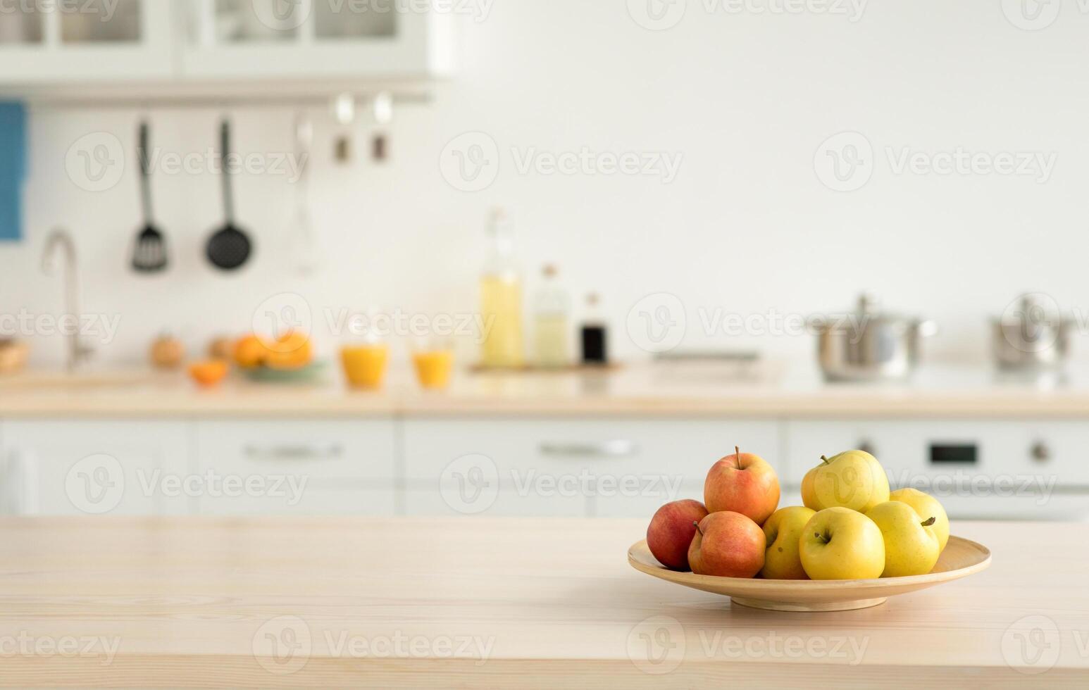 Cozy home kitchen design and comfortable style, ad for rent. Plate with apples on table, bottles of sauces and utensils, orange juice in glasses and fruits, light walls and white furniture, copy space photo
