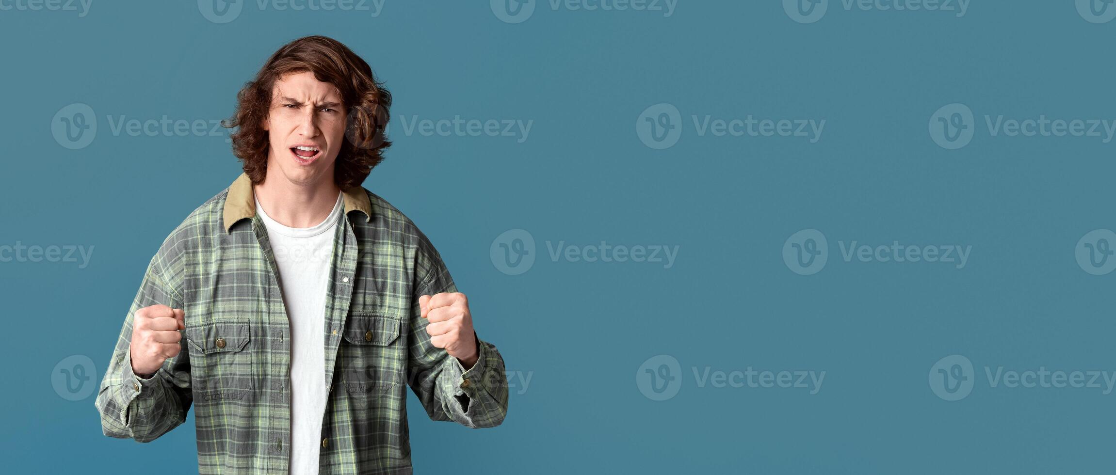 Conflict concept. Furious millennial guy clenching fists on color background photo