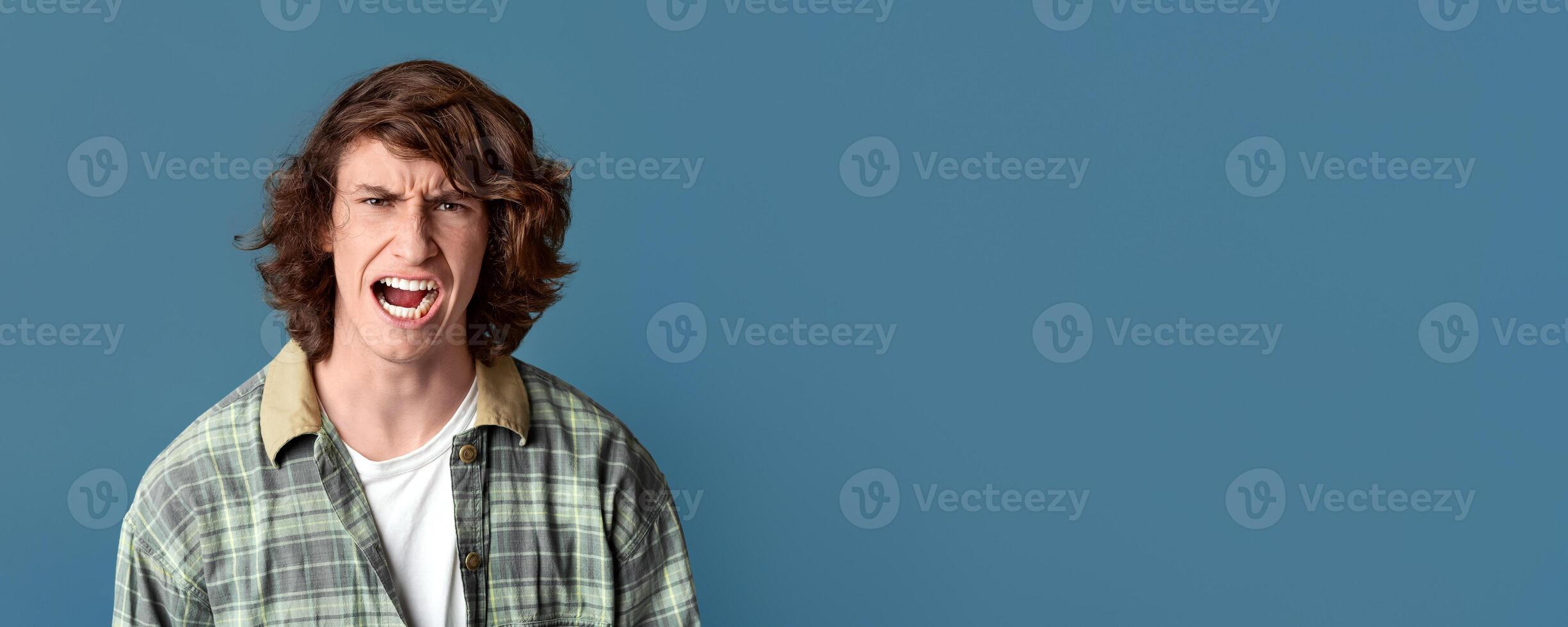 Expressing anger. Young guy with furious facial expression on turquoise background photo