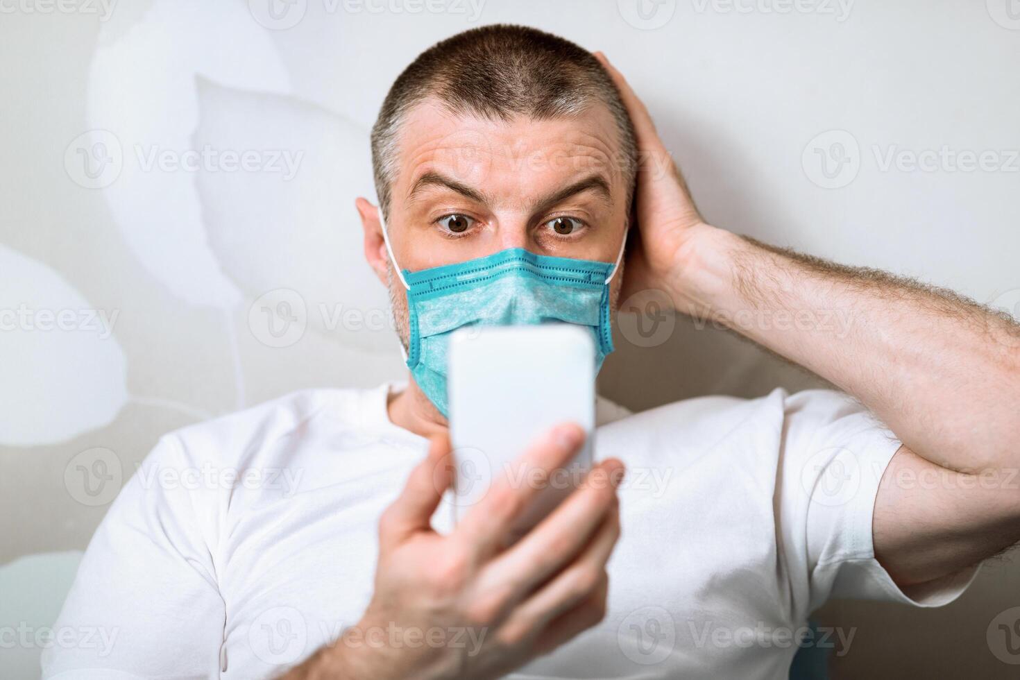 Coronavirus Anxiety. Scared Man In Protective Mask Using Phone Reading Shocking News About Pandemic Outbreak Sitting At Home. Selective Focus photo