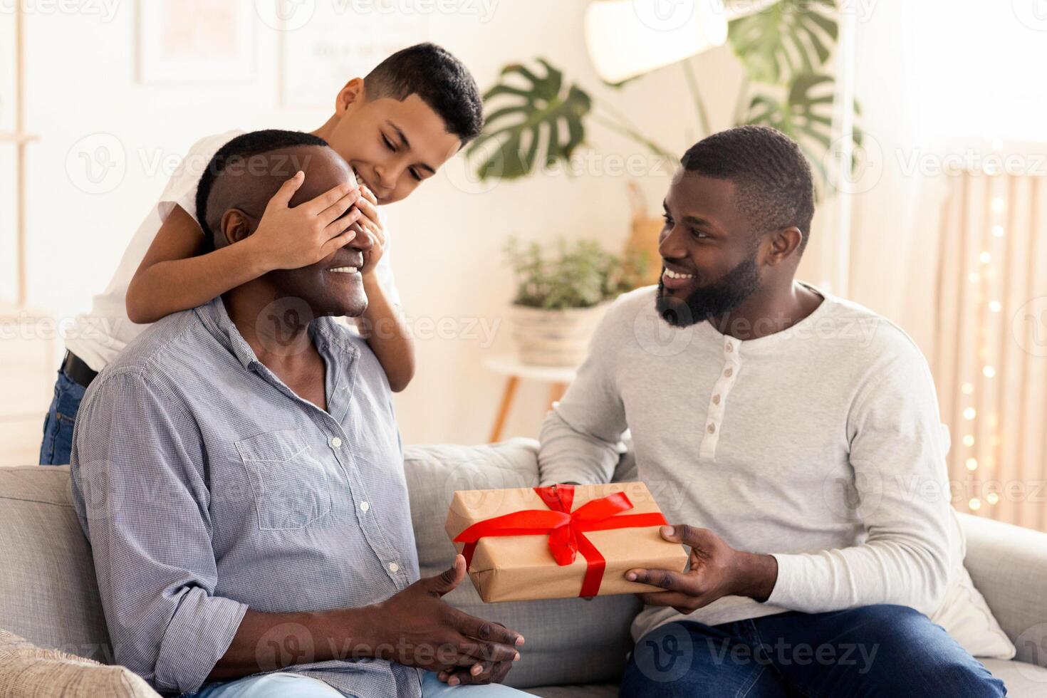 Grandfather's Birthday. Affectionate Little Boy And His Father Surprising Happy Granddad With Gift At Home, Congratulating With Anniversary photo