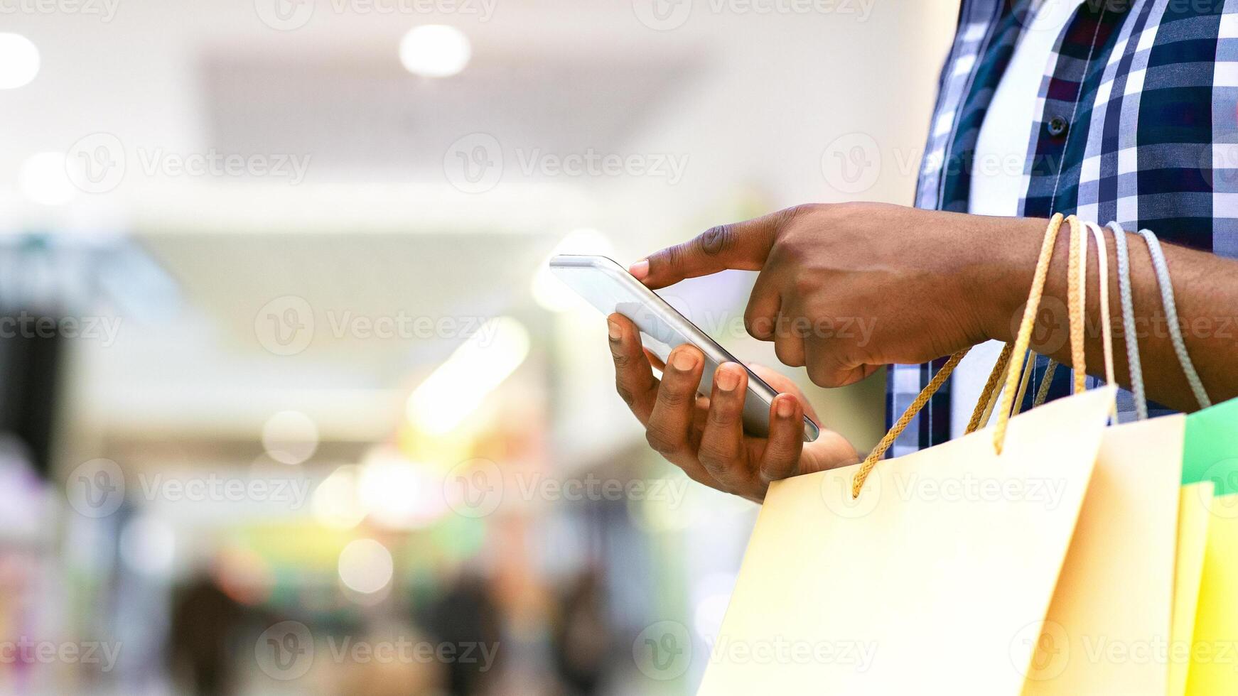 Unrecognizable African Man Carrying Shopping Bads And Using Smartphone In Mall, Cropped Image With Copy Space photo